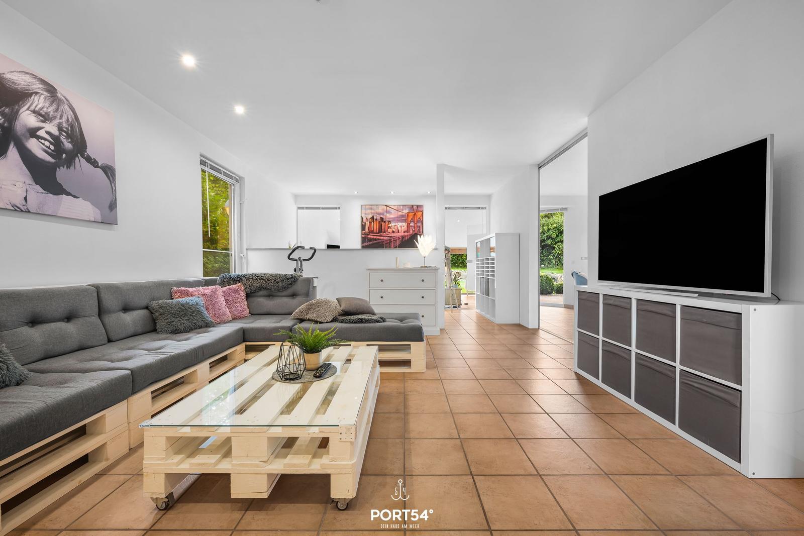 Wohnzimmer mit Sofa aus Paletten, Glas-Tisch und Fernseher.