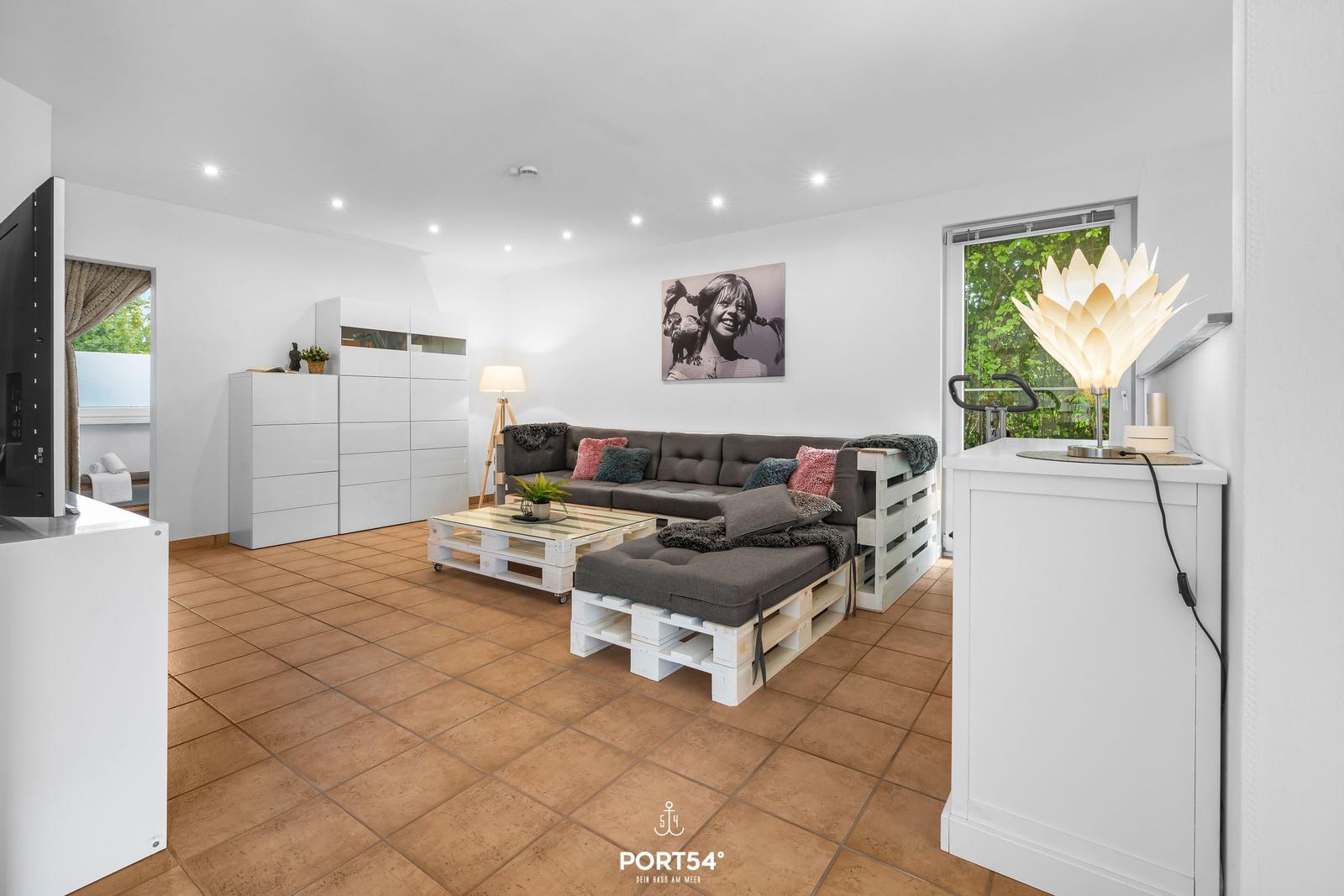 Wohnzimmer mit Sofa aus Paletten, Glas-Tisch und Wandbild.