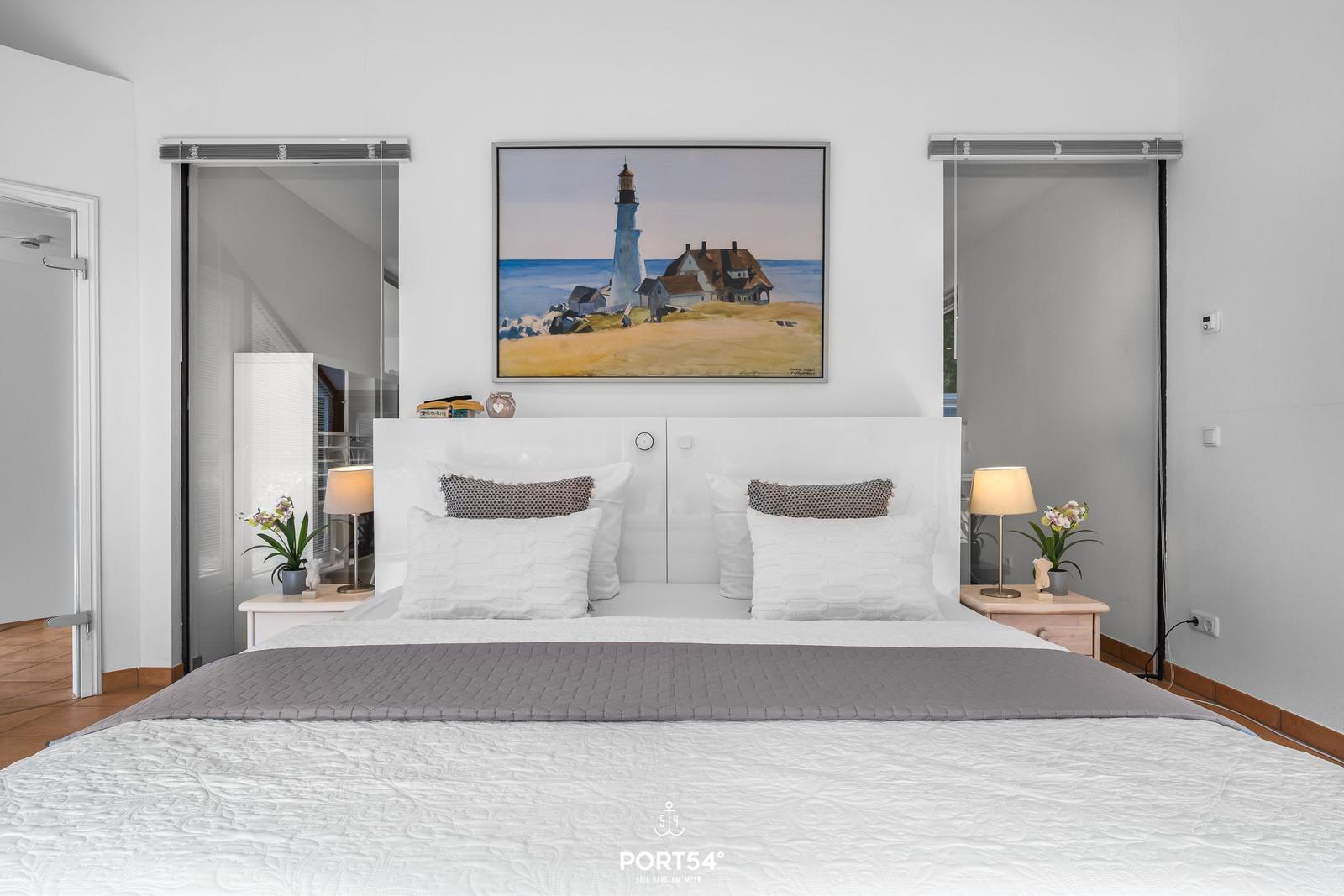 Schlafzimmer mit Bett, Nachttischen und Wandbild mit Leuchtturm.