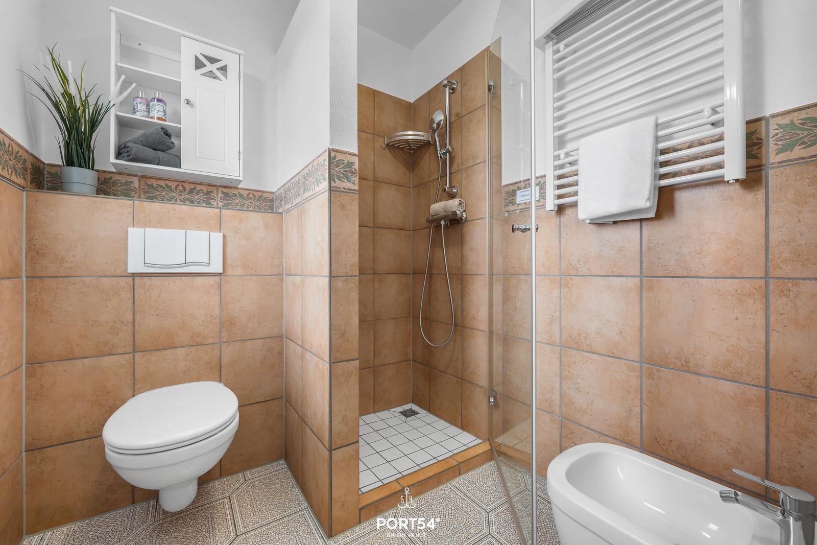 Badezimmer mit Dusche, Badewanne und Toilette. Wandfliesen und Mosaikboden.