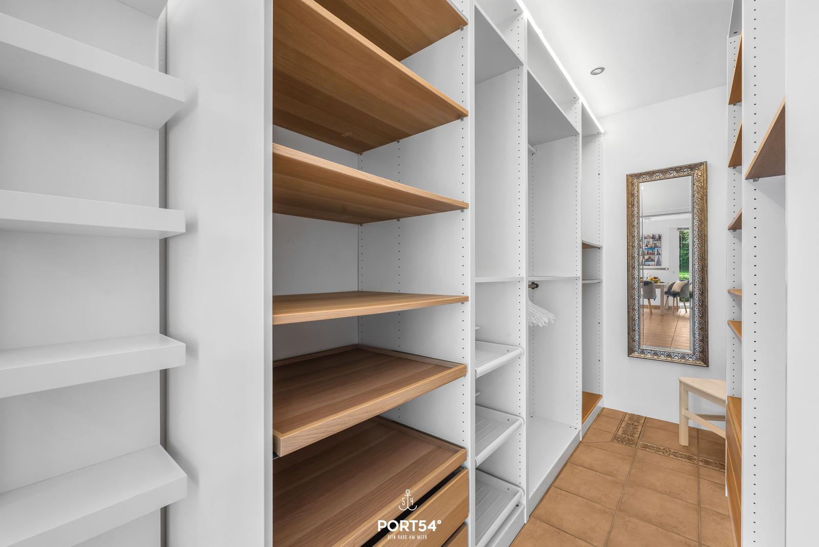 Großer Kleiderschrank mit Holzregalen und Spiegel an der Wand.