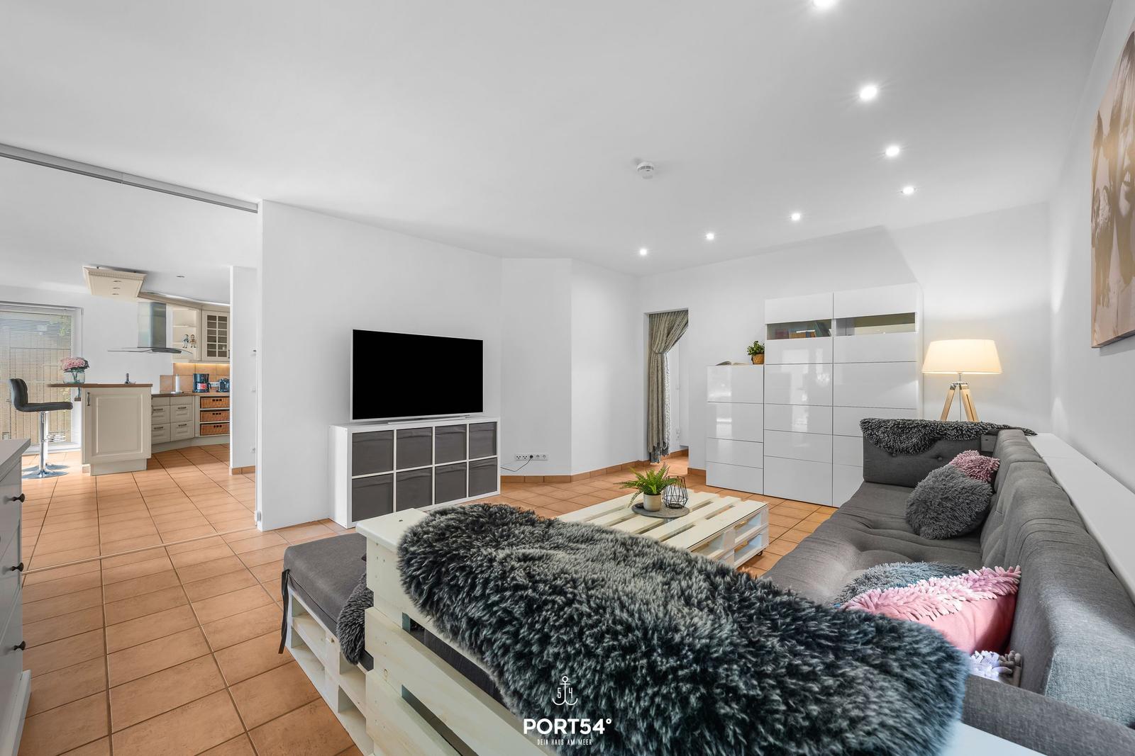 Wohnzimmer mit Sofa, Fernseher und Küchenbereich im Hintergrund.