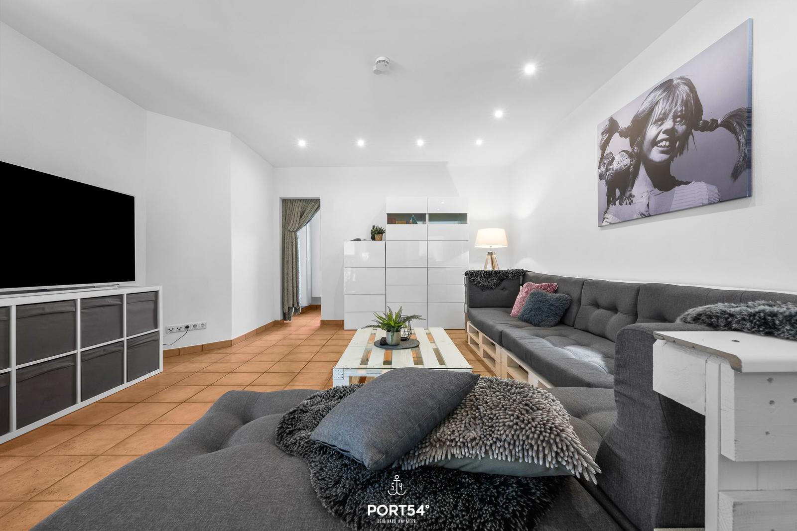 Wohnzimmer mit grauem Sofa, Fernseher und Wandbild.