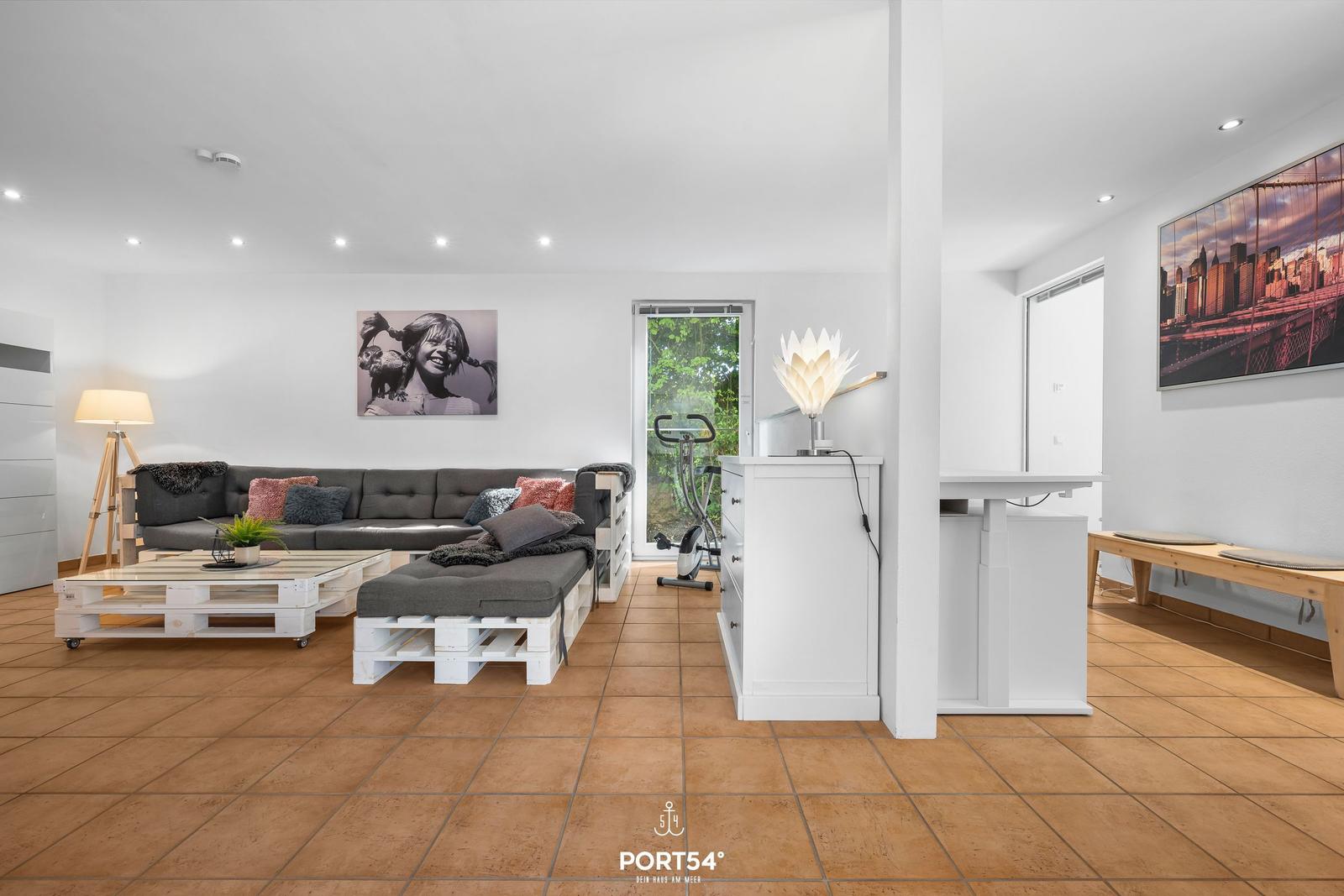 Wohnbereich mit Sofa, Couchtisch und Fitnessgerät. Wandbild und Holzboden.