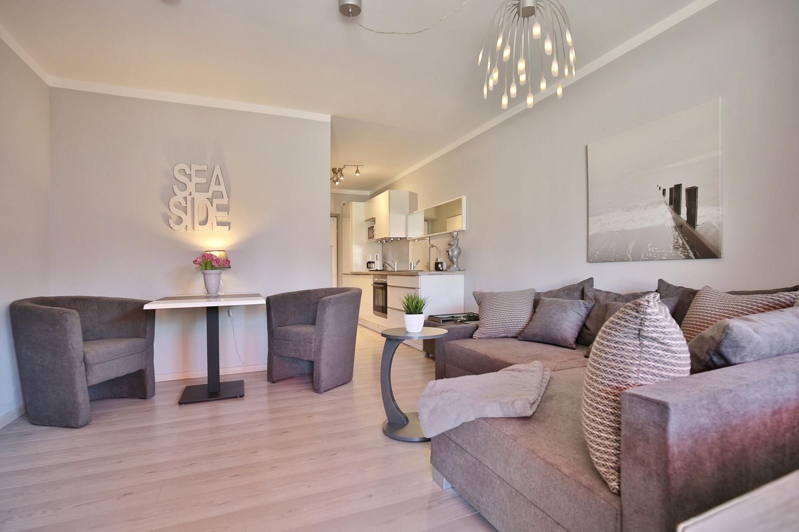 Wohnzimmer mit Sofa, zwei Sesseln und Küchenbereich im Hintergrund.