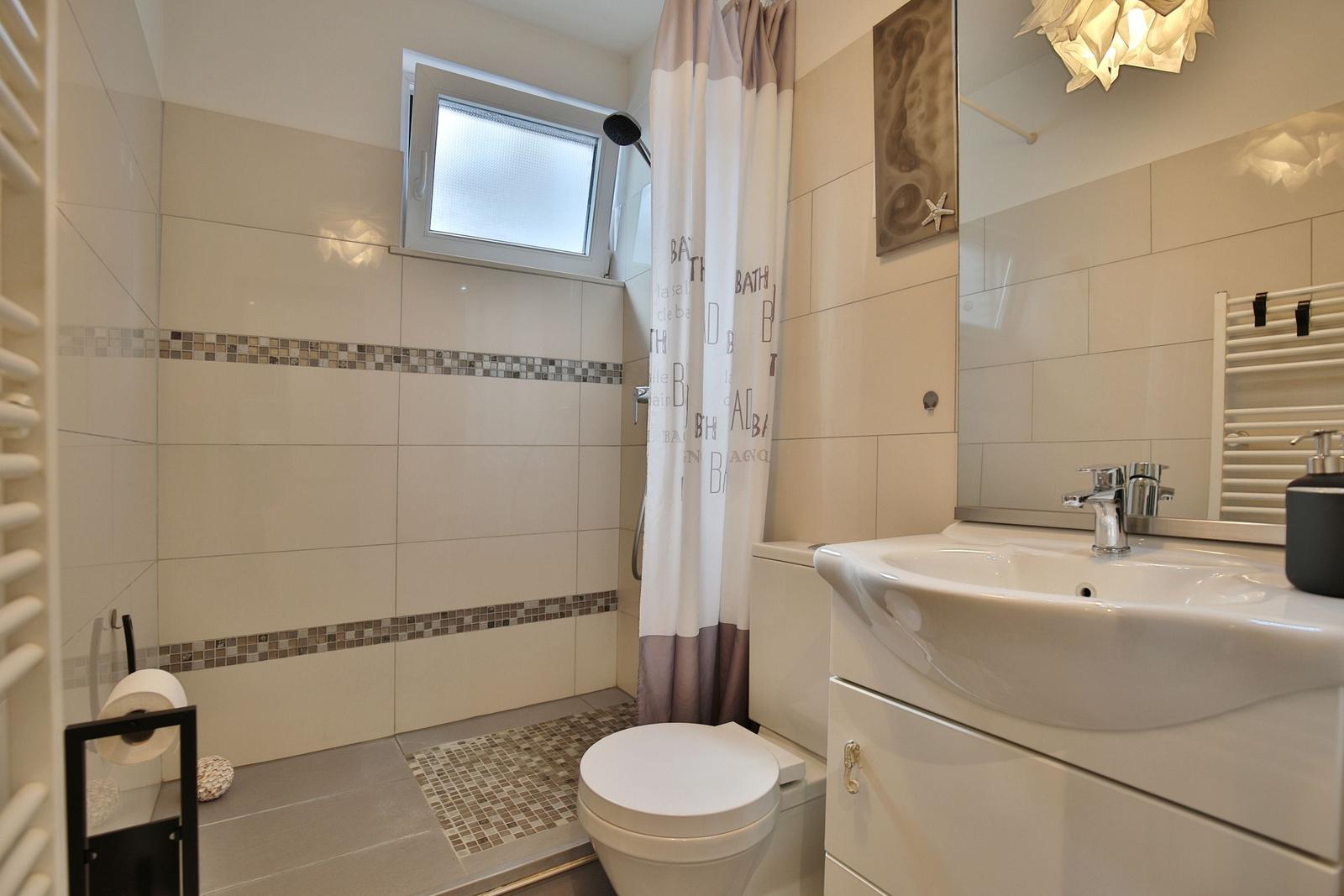 Badezimmer mit Dusche, Waschbecken und Toilette. Fliesen und Mosaikverkleidung.