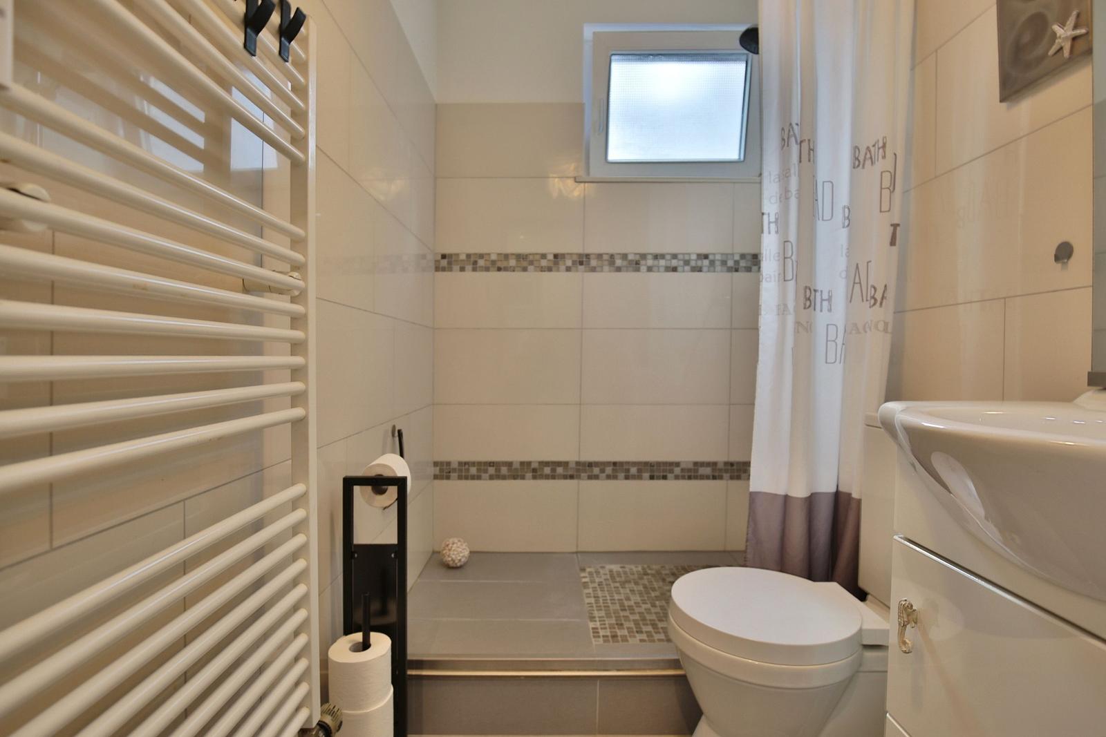 Badezimmer mit Dusche, Toilette und Waschbecken. Fliesen und Duschvorhang sichtbar.