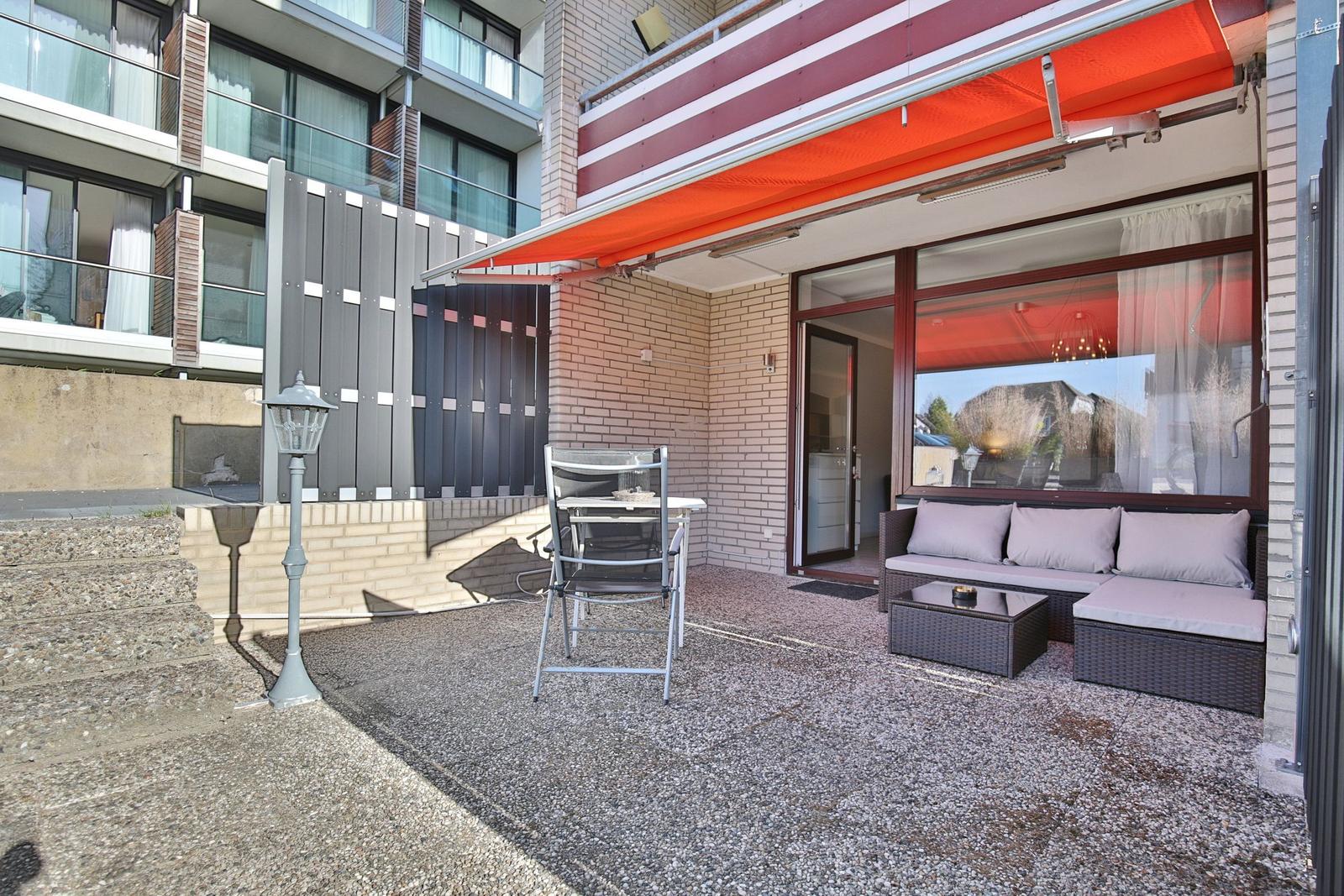 Terrasse mit Sitzgruppe, Tisch, Stuhl und orangefarbenem Markisenüberdachung.