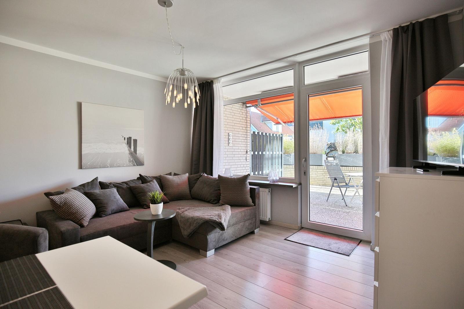 Wohnzimmer mit Sofa, Glasfront und Balkon mit Sonnenschutz.