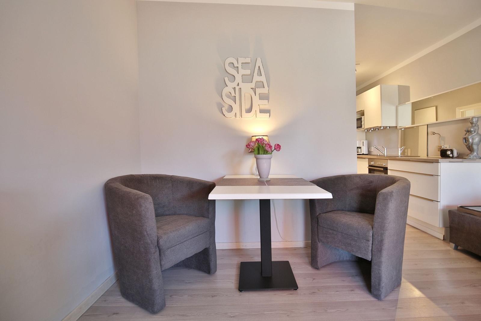 Essbereich mit zwei Sesseln und Tisch. Küchenbereich im Hintergrund.