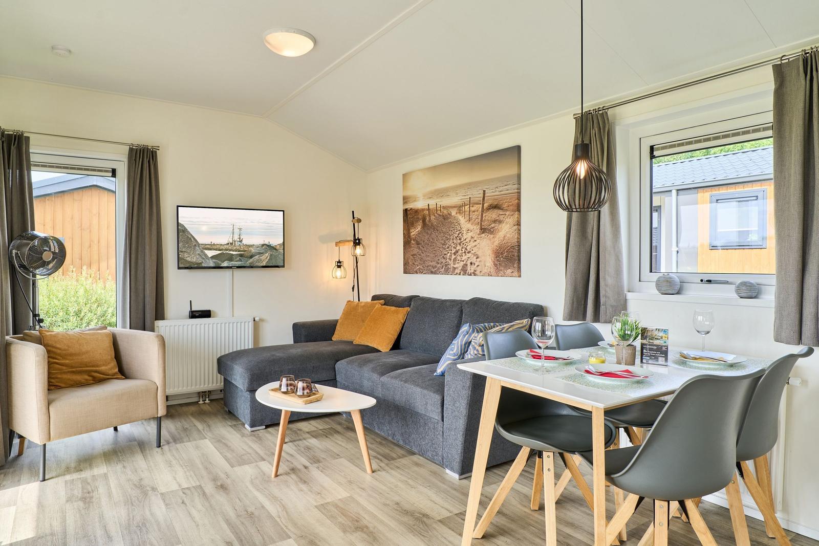 Wohn- und Essbereich mit Sofa, Tisch und TV. Fenster mit Vorhängen.