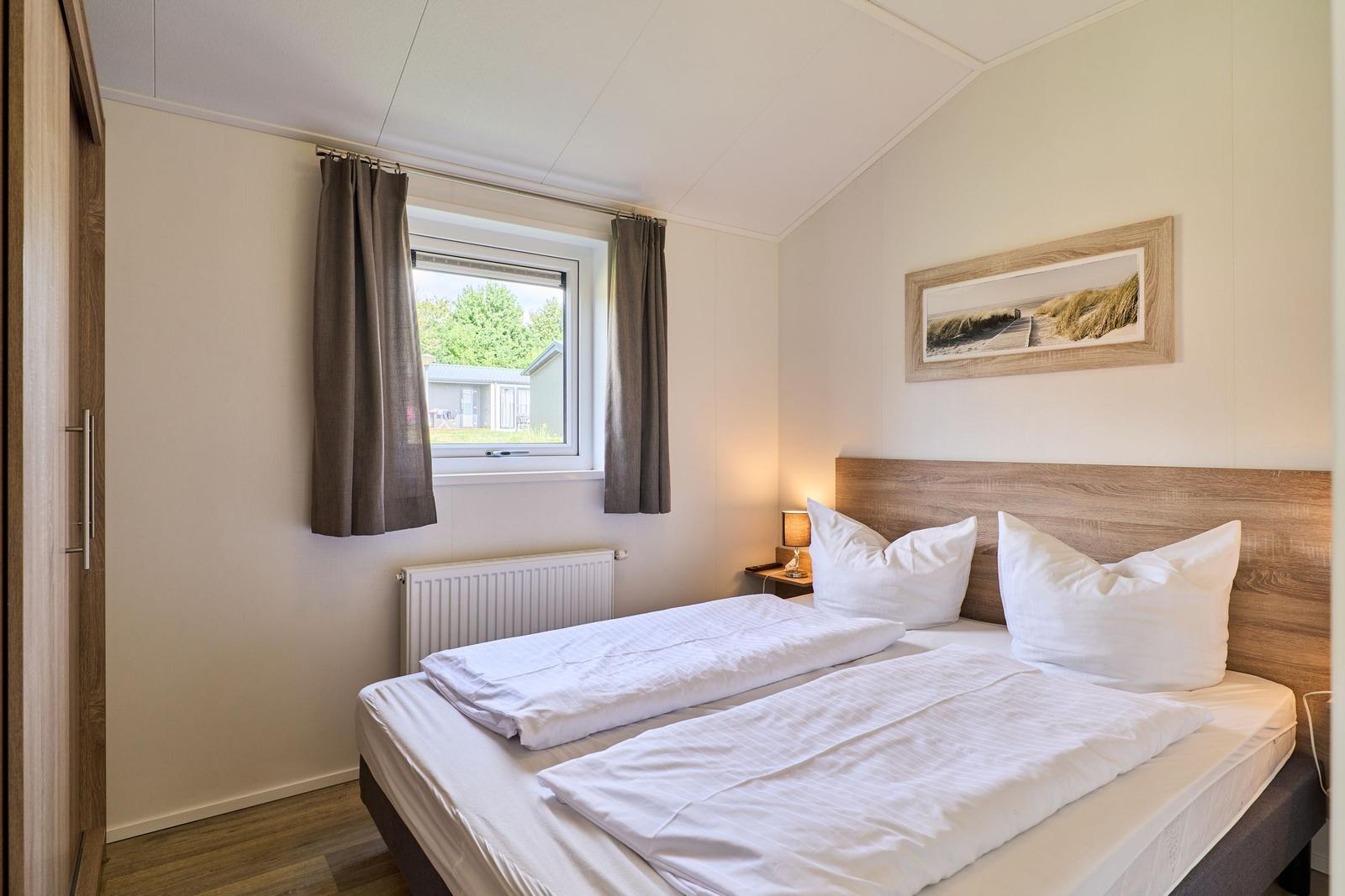 Schlafzimmer mit Doppelbett, Fenster und Wandbild.