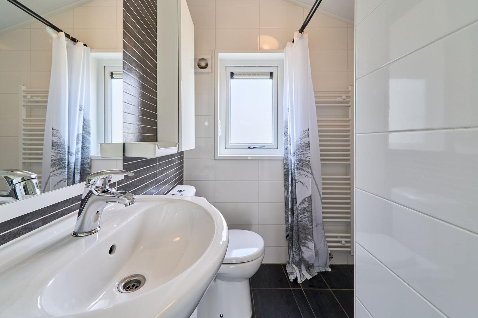 Badezimmer mit Waschbecken, Toilette und Duschbereich mit Fenster.