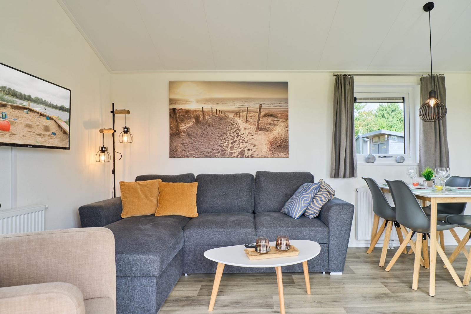 Wohnzimmer mit Sofa, Couchtisch und Essbereich. Wandbild und TV sichtbar.