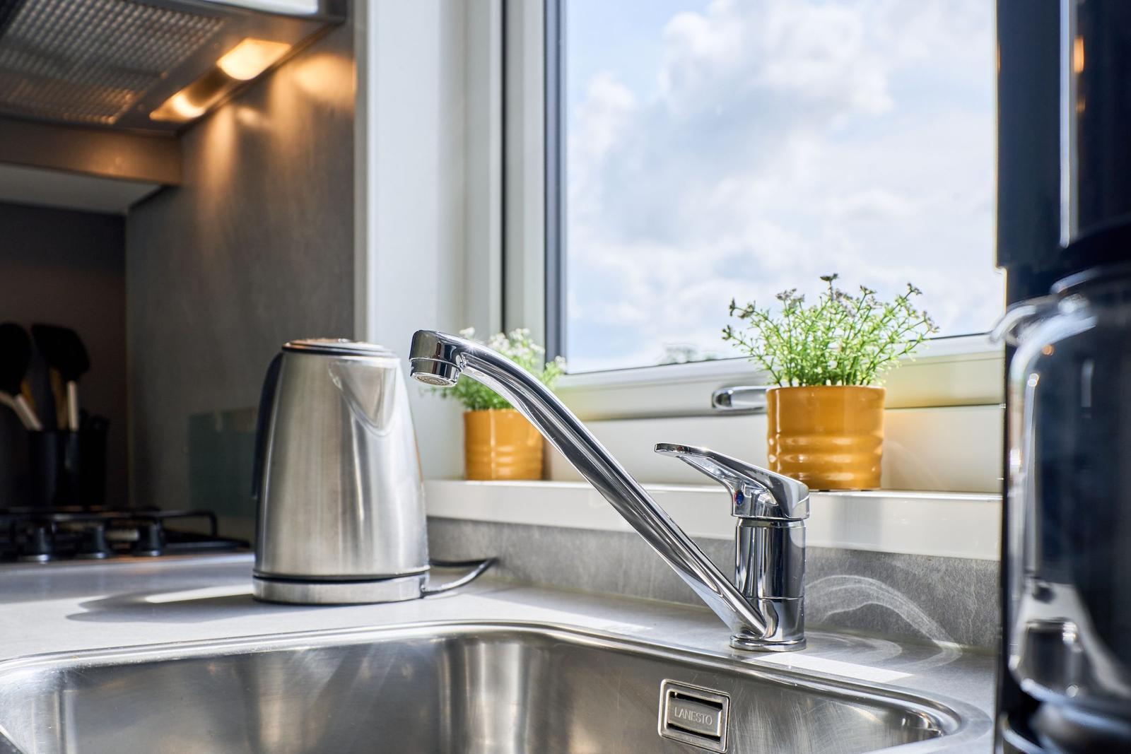 Küchenzeile mit Wasserhahn, Kanne und Pflanze am Fenster