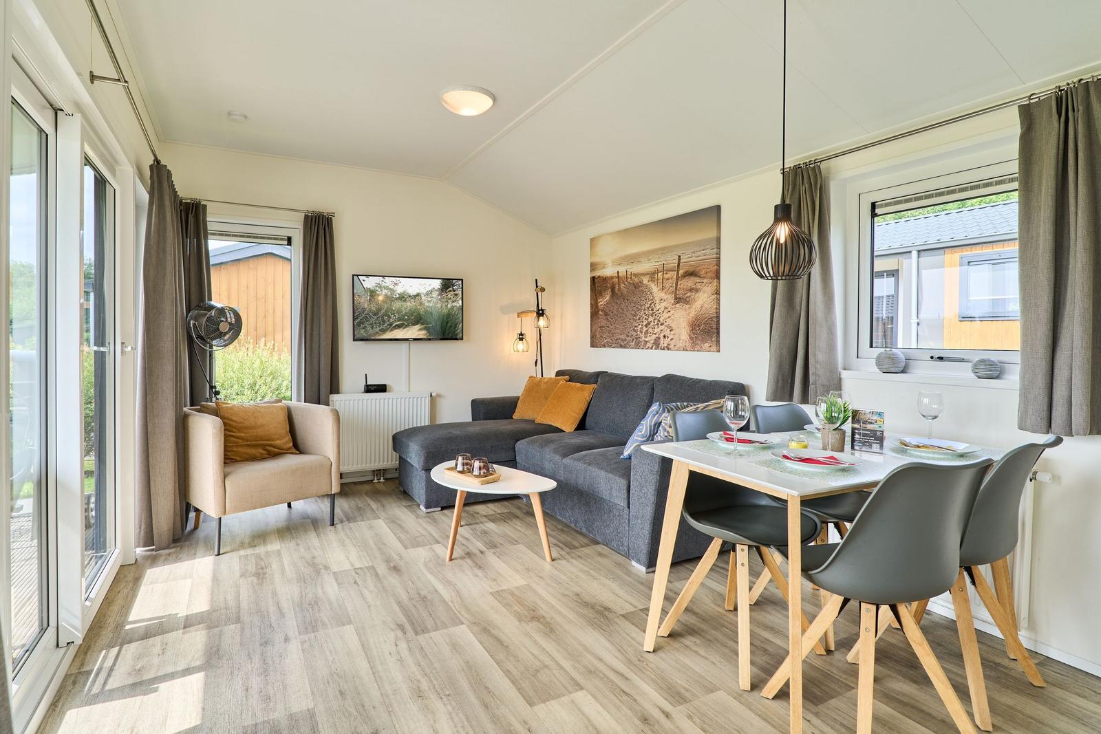 Wohn- und Essbereich mit Sofa, Tisch und Stühlen. Fenster und Tür führen nach draußen.