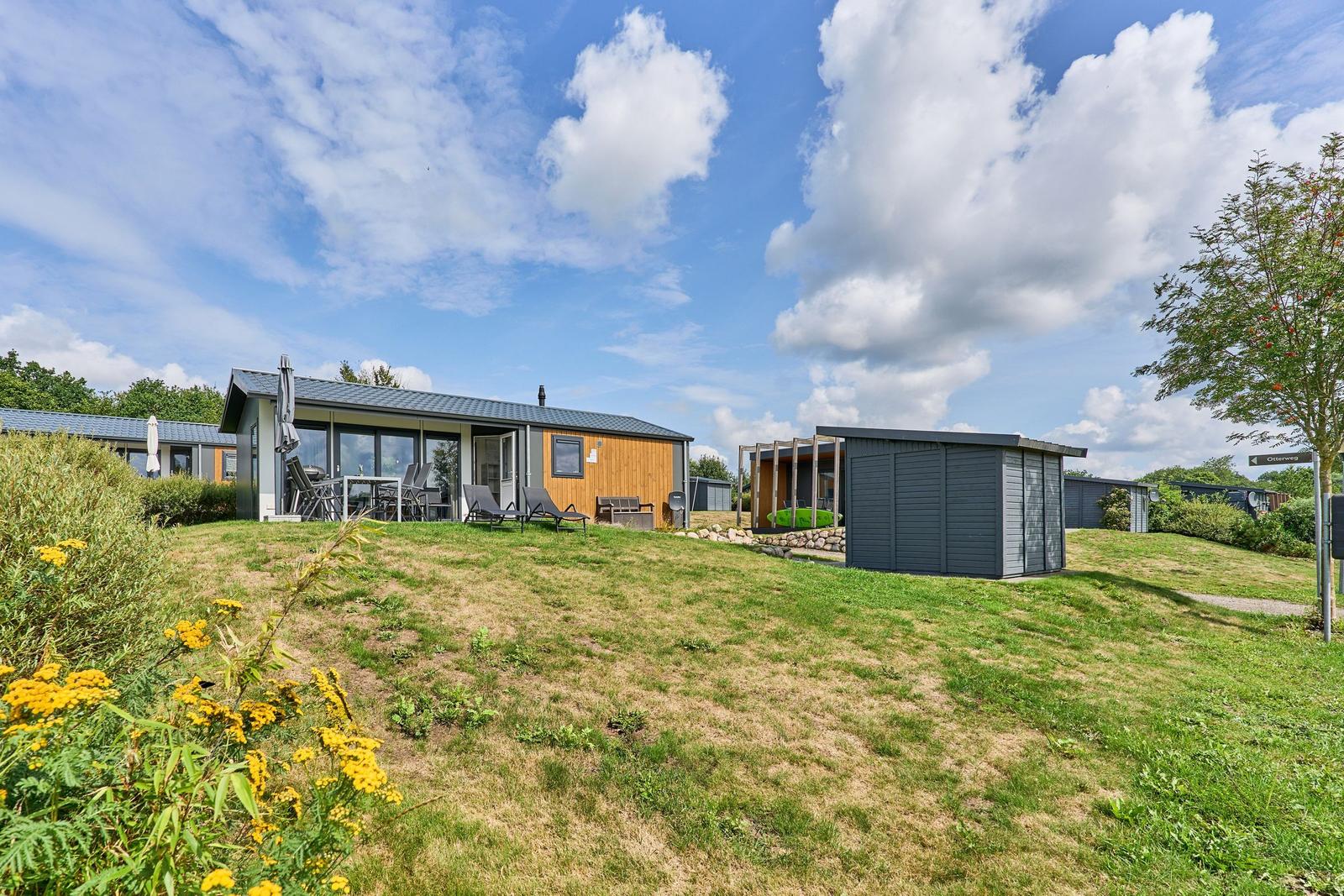 Moderne Ferienhaus mit Terrasse, Liegen und Garten unter blauem Himmel.