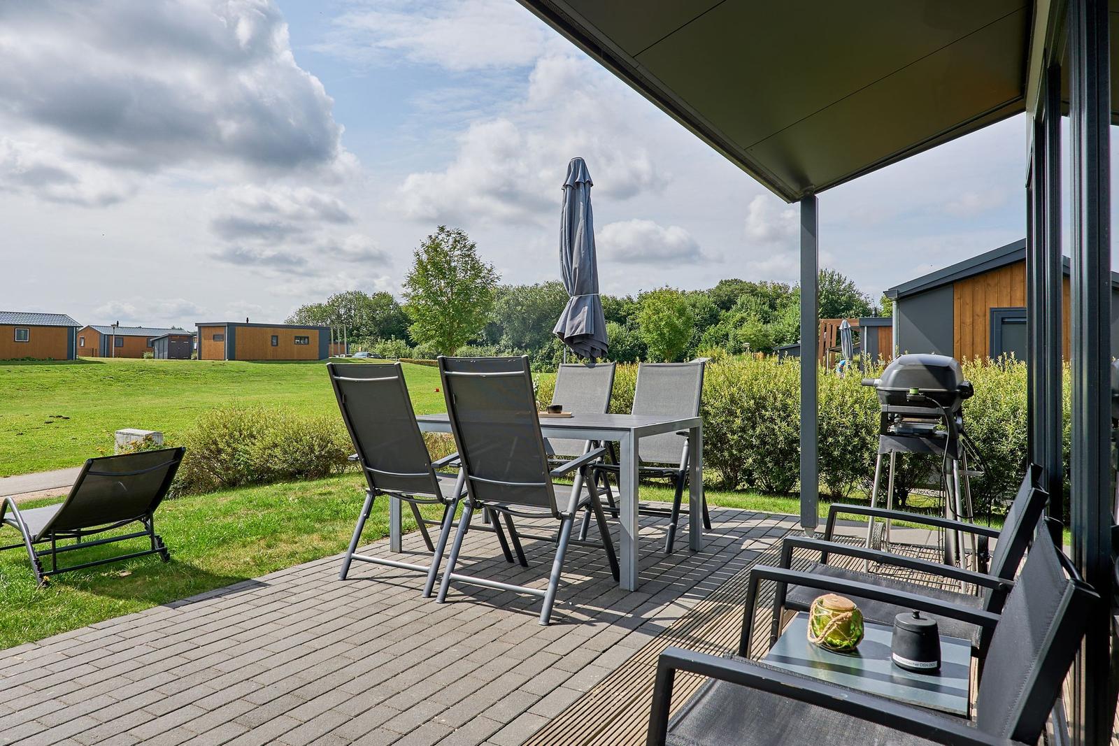 Terrasse mit Tisch, Stühlen und Grill. Blick auf Grasfläche und Bäume.