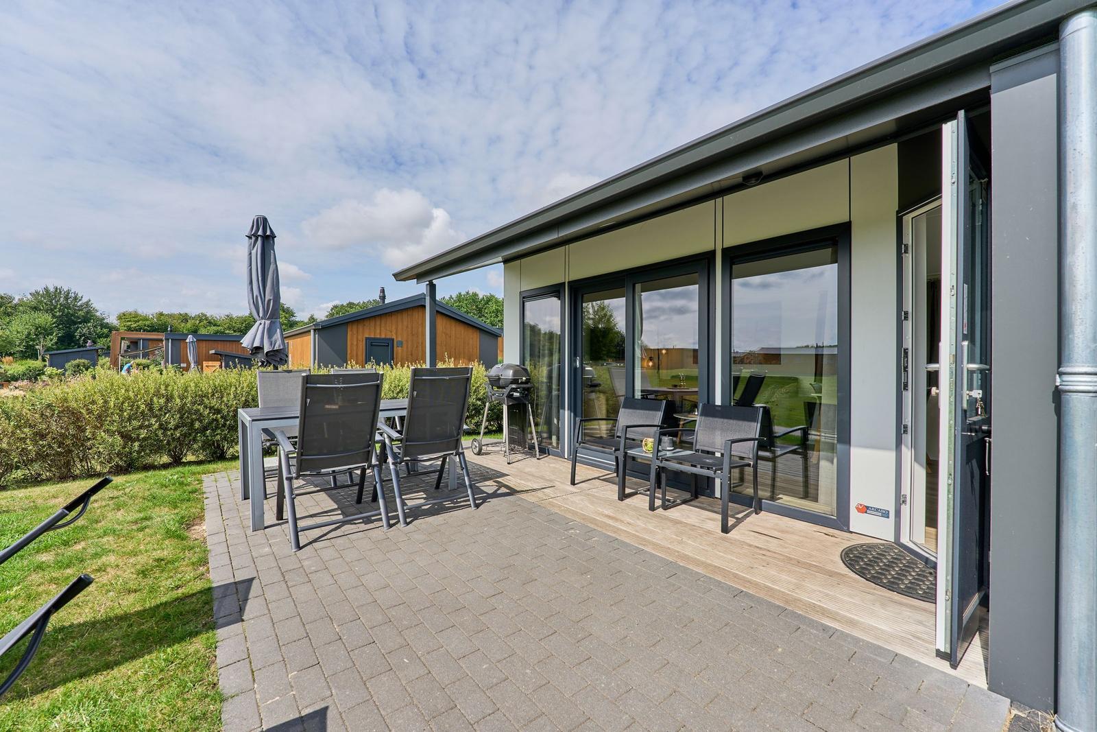 Terrasse mit Sitzgruppe, Grill und Gartentisch. Hinterhof mit Rasen und Hecken.