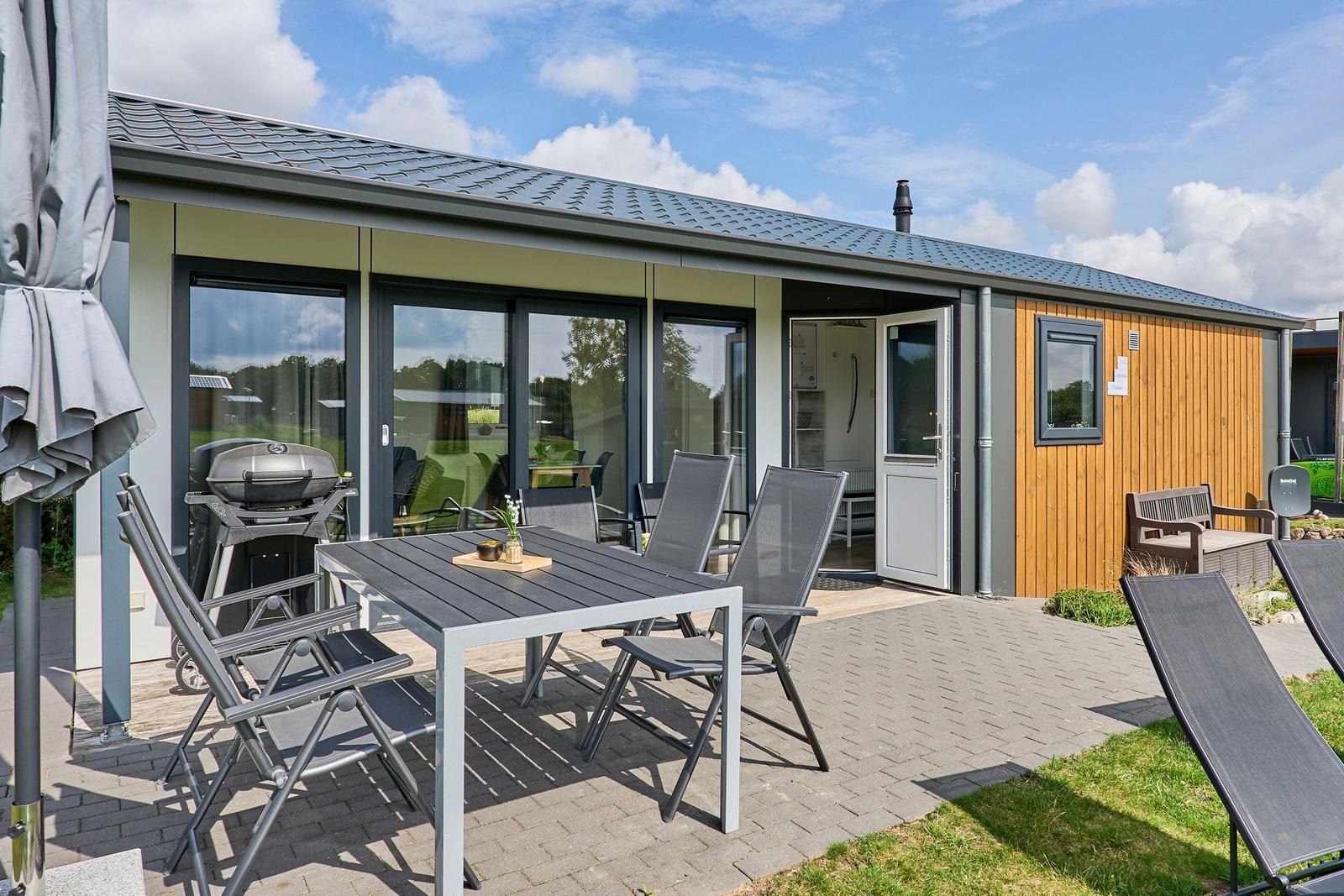 Terrasse mit Tisch, Stühlen und Grill. Eingang und Fenster sind sichtbar.