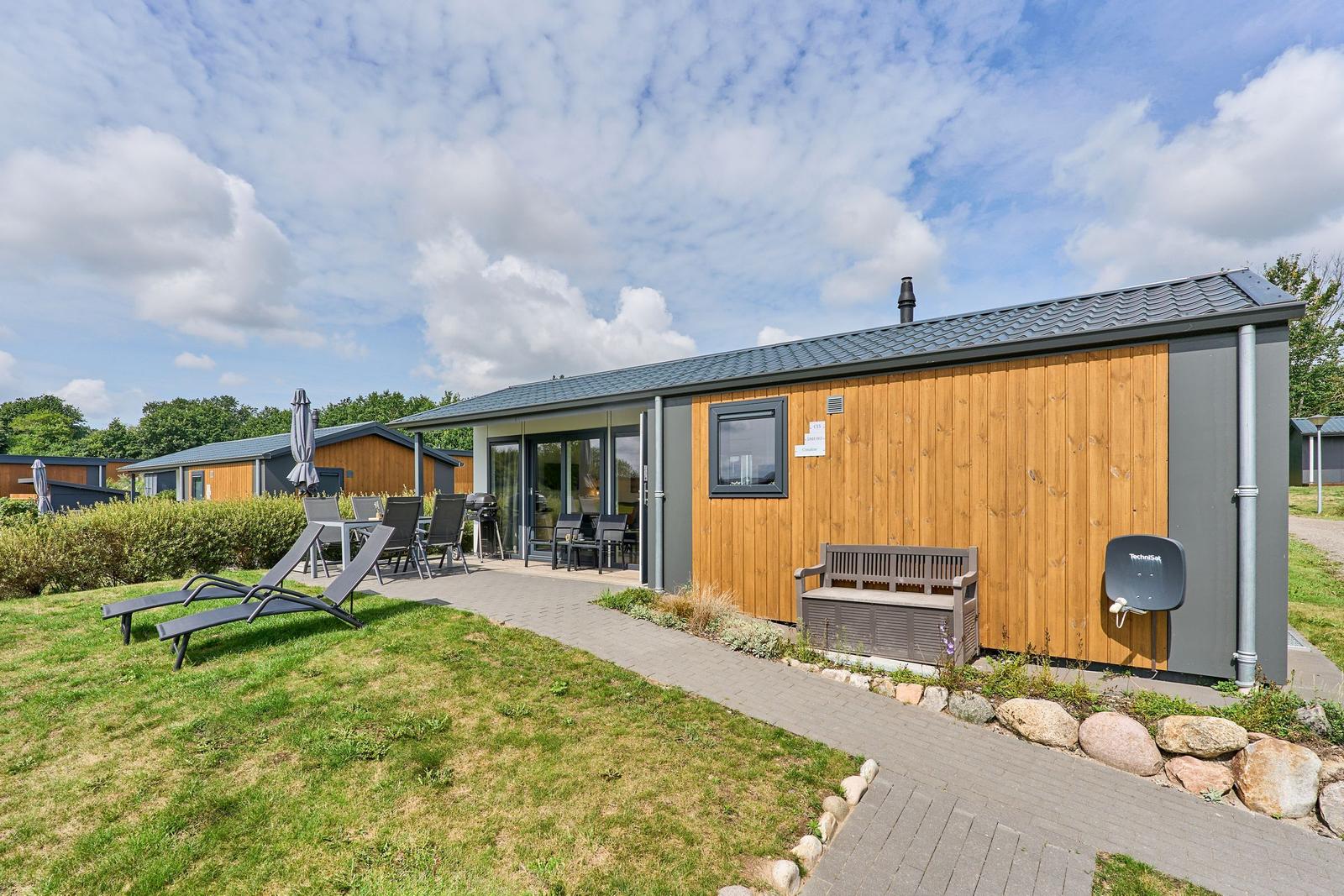 Moderne Ferienhaus mit Terrasse, Liegen und Grillplatz im Freien.