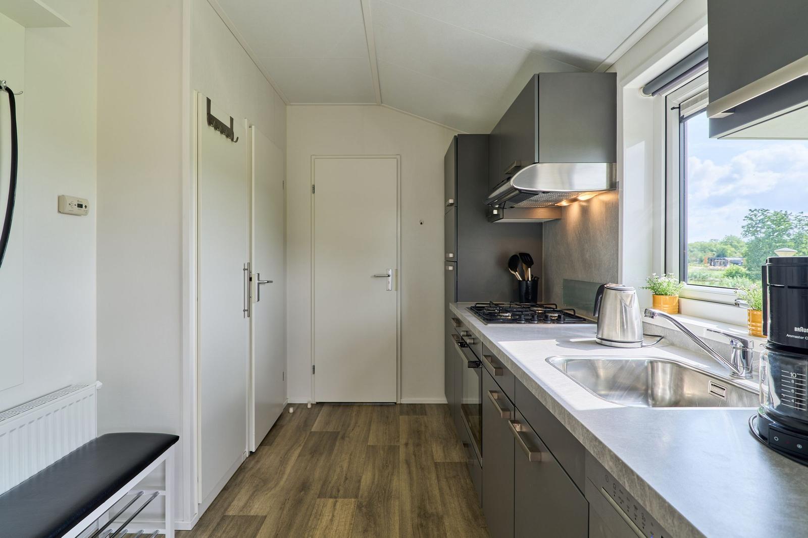 Küche mit Arbeitsplatte, Spüle und Fenster. Holzboden und graue Schränke.