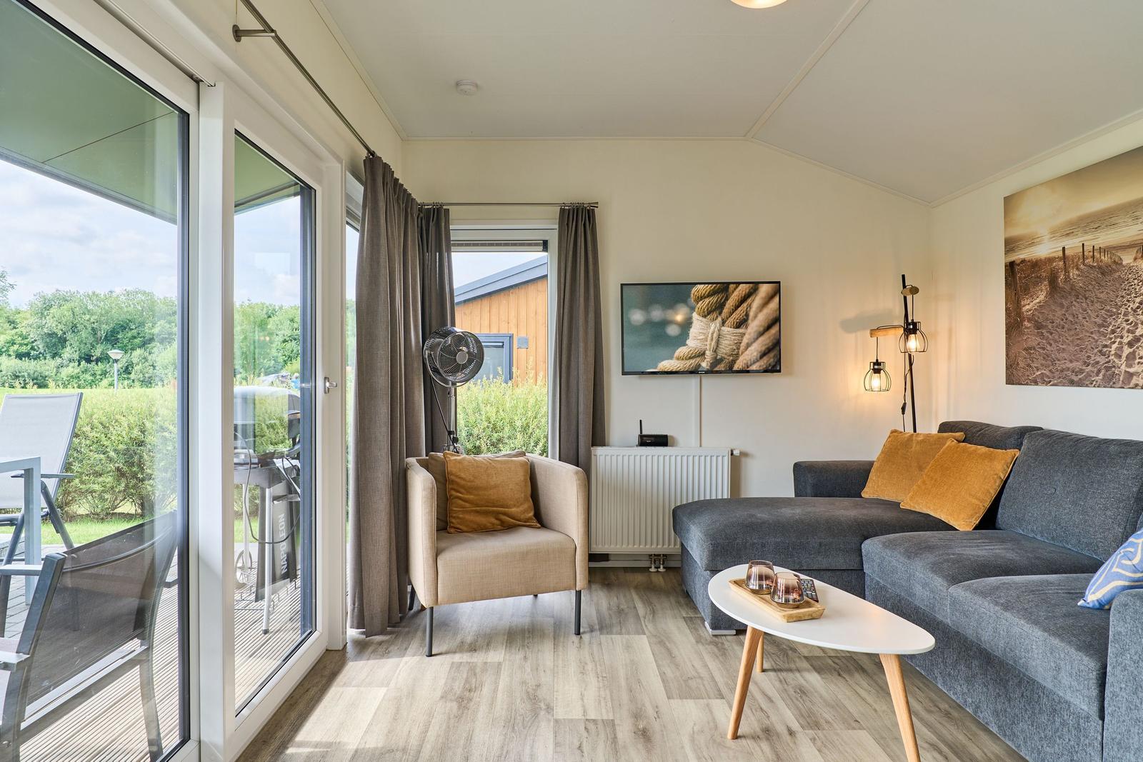 Wohnzimmer mit Sofa, Sessel und TV. Durchgang zur Terrasse mit Gartenansicht.