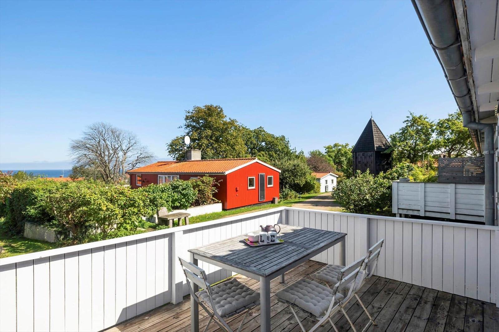Terrace with table and chairs. View of red house and sea.