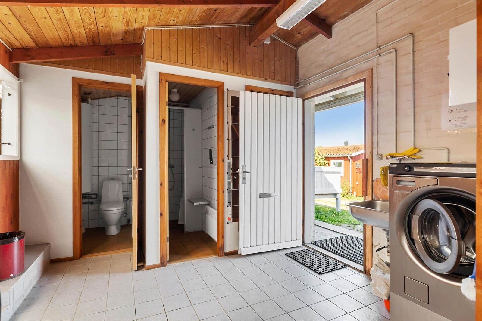 Utility room with washing machine, toilet, and shower. Outdoor view through open door.