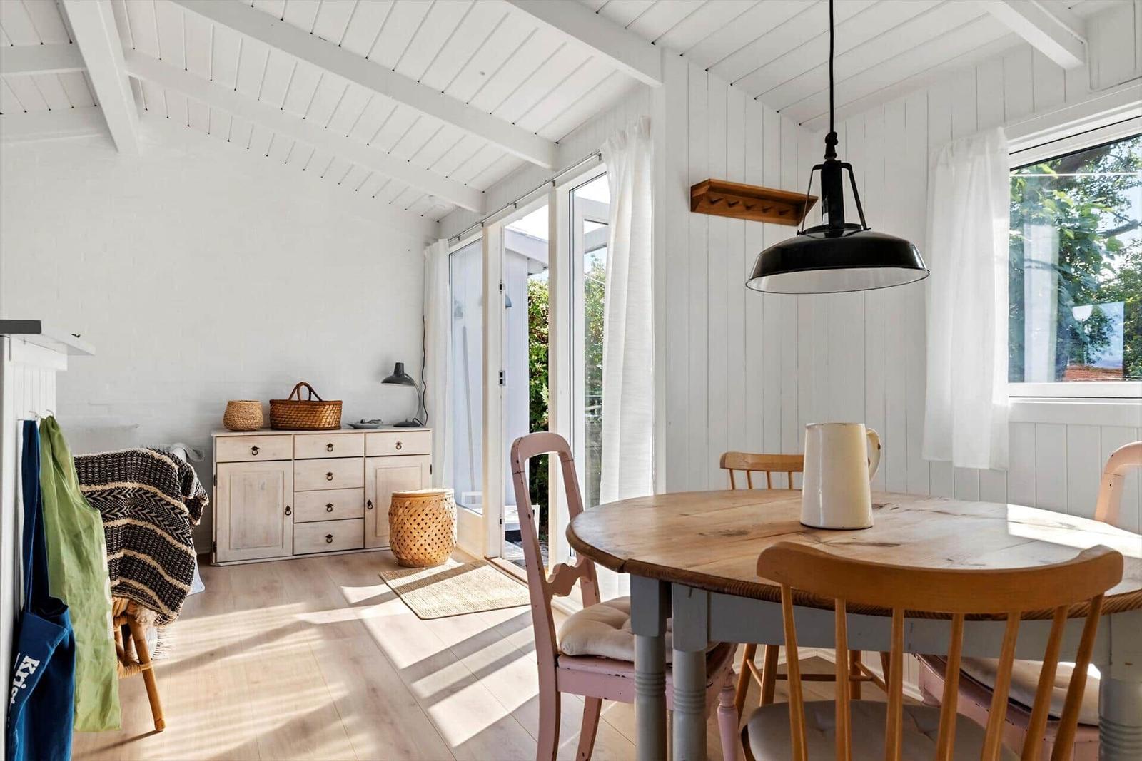 Dining area with wooden table, chairs, and windows to the outdoor terrace.