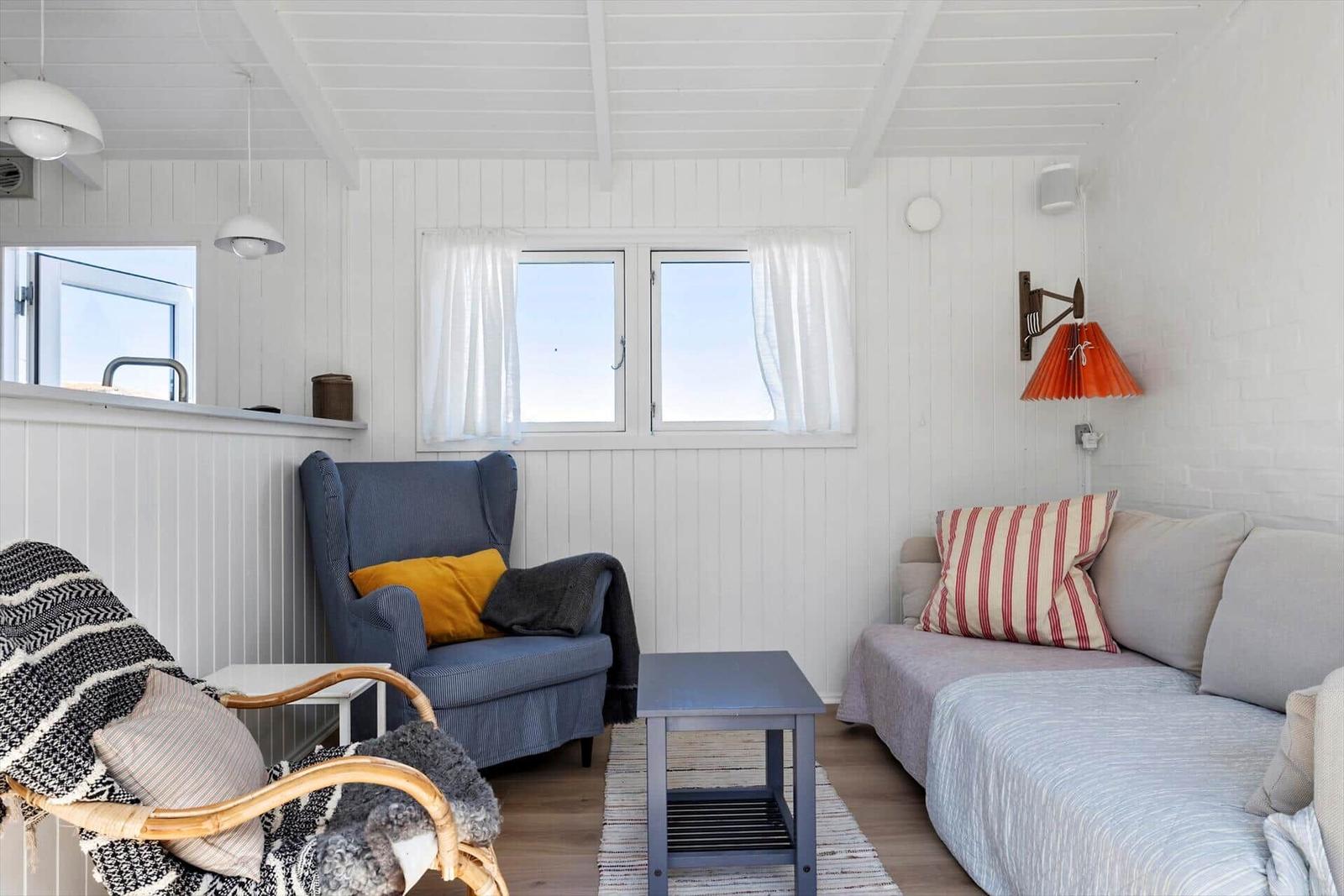 Living room with sofa, armchair, and table. Windows and white walls.