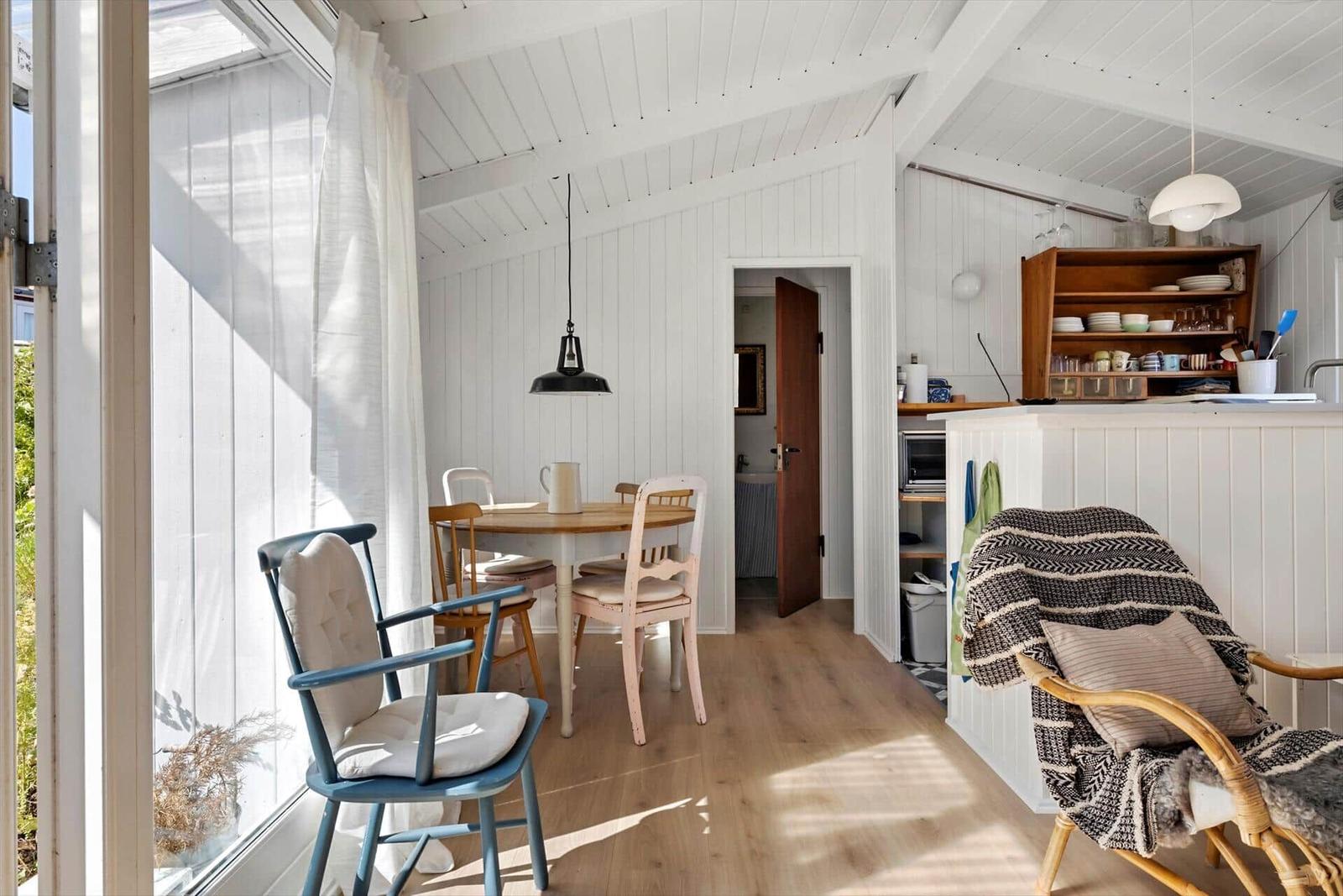 Kitchen and dining area with wooden floor and white walls. A window with curtain and chairs.