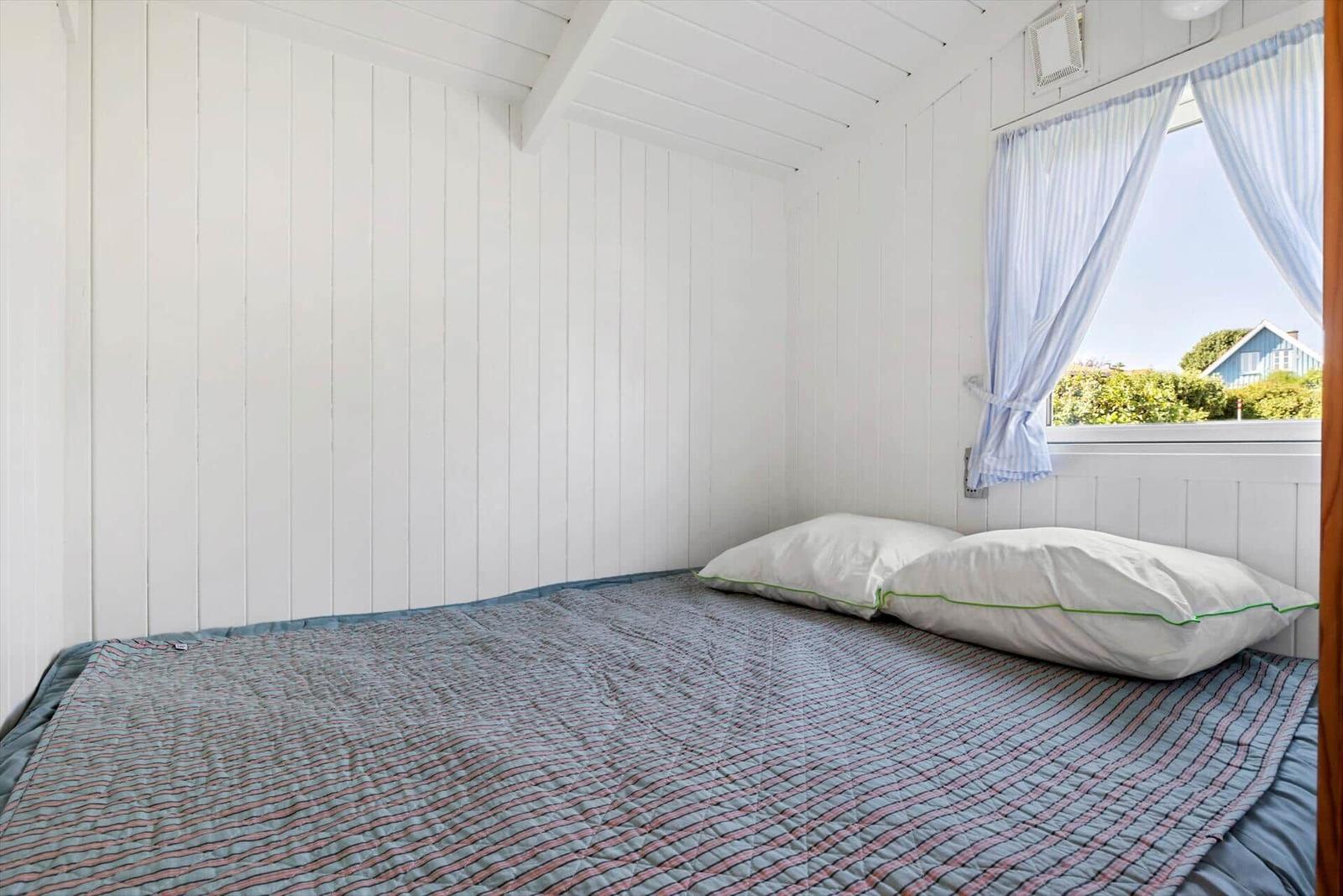Bedroom with bed, white walls, and window with curtains.
