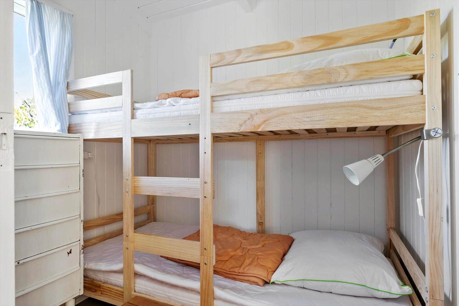 Room with two bunk beds, wooden frame, white dresser, and window with curtain.