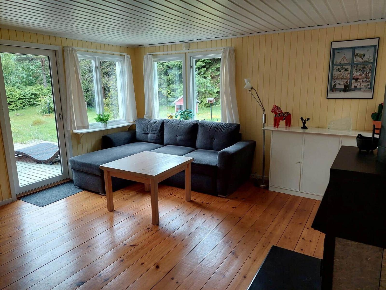 Wohnzimmer mit Sofa, Tisch und Fenstern zum Garten.