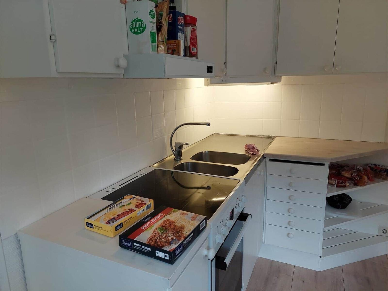 Küche mit Spüle, Herd und Schränken. Auf Arbeitsfläche liegen Nudelboxen.