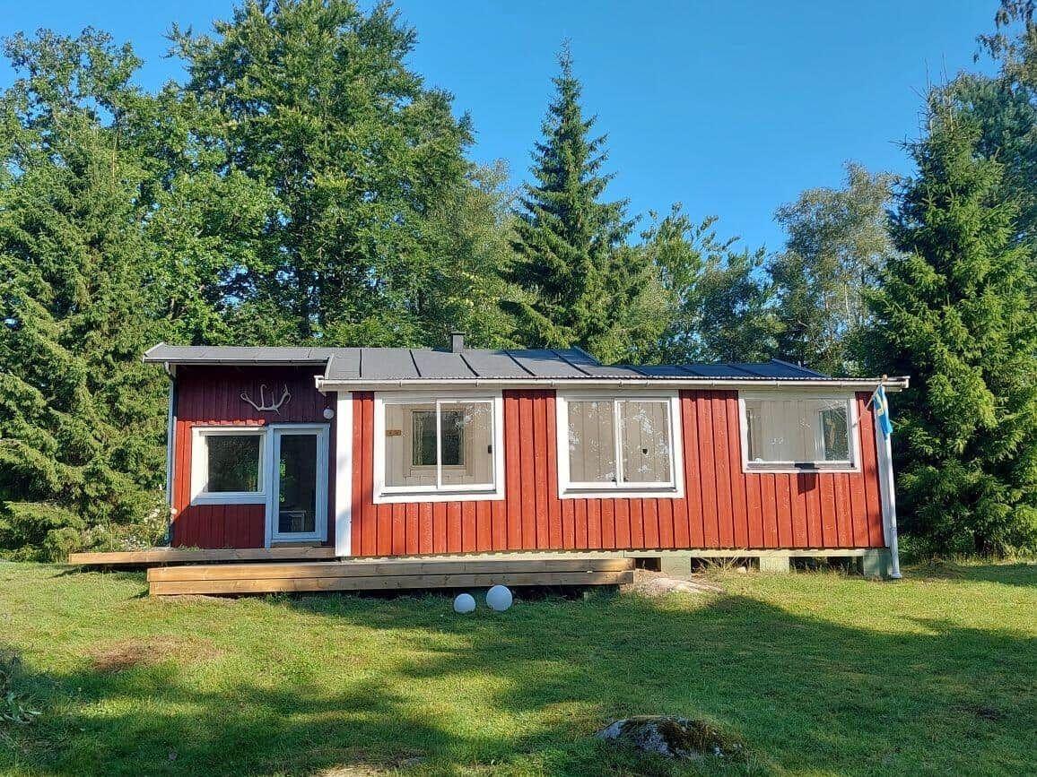 Rotes Holzhaus mit Terrasse und Fenstern, umgeben von Bäumen und Gras.