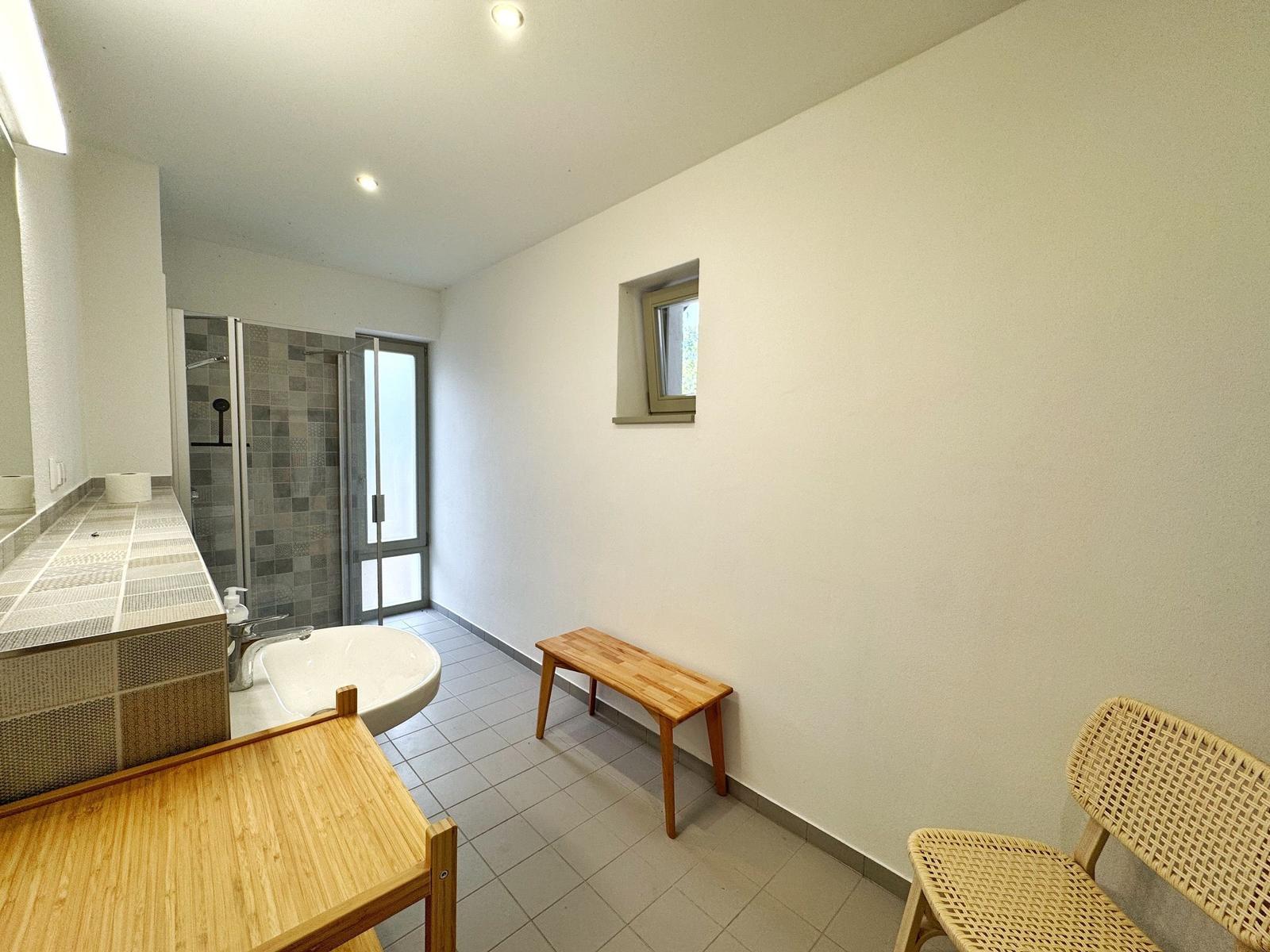 Badezimmer mit Dusche, Waschbecken und Holzbank.