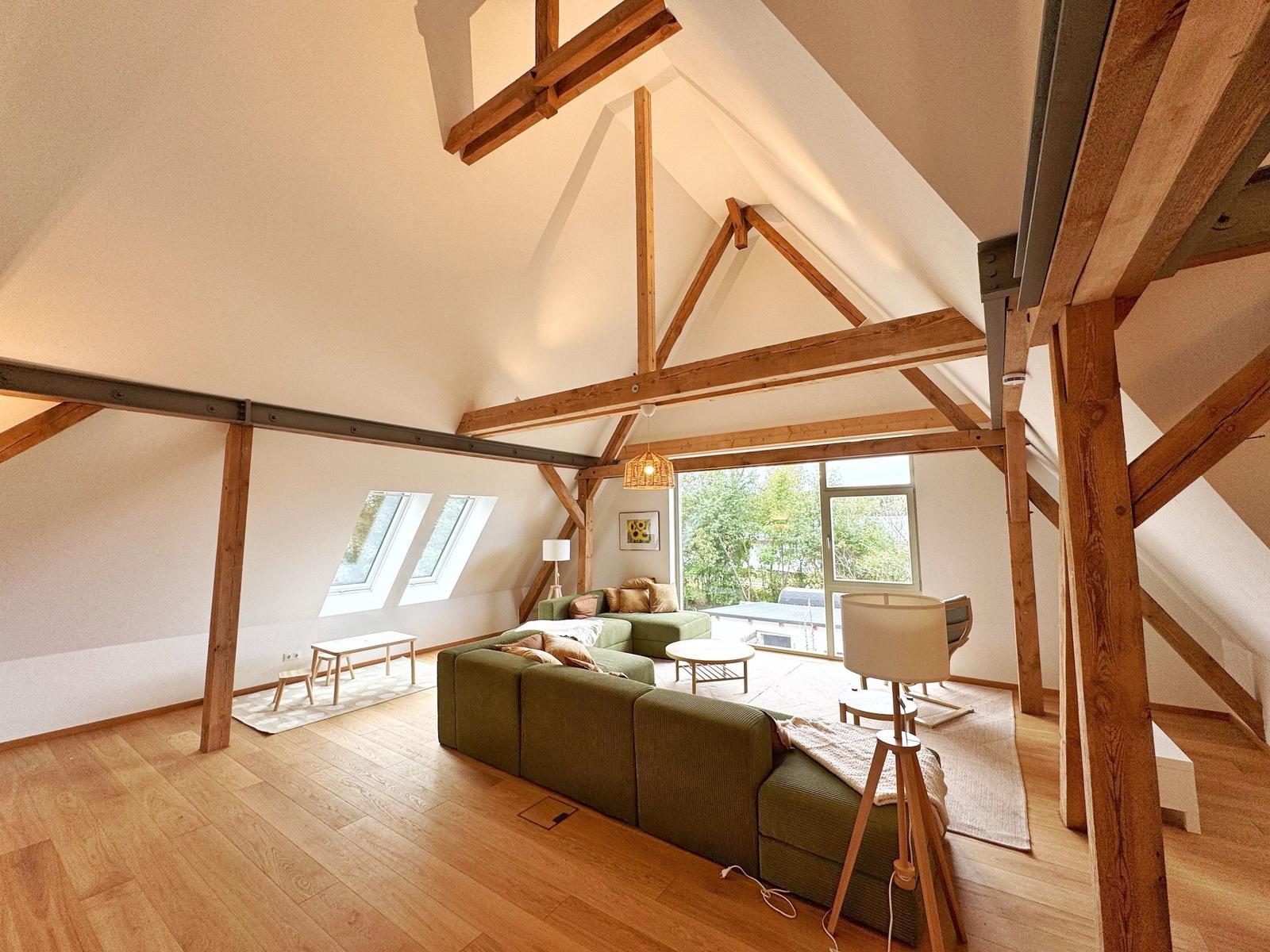 Wohnraum mit Holzdecke, Sofa und Fenster zur Außenterrasse.