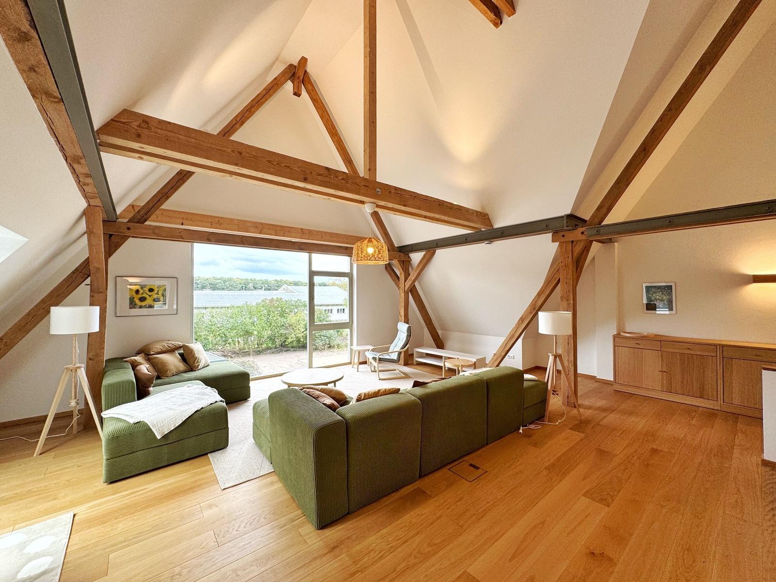 Großes Wohnzimmer mit grünen Sofas, Holzboden und Holzbalken an der Decke.