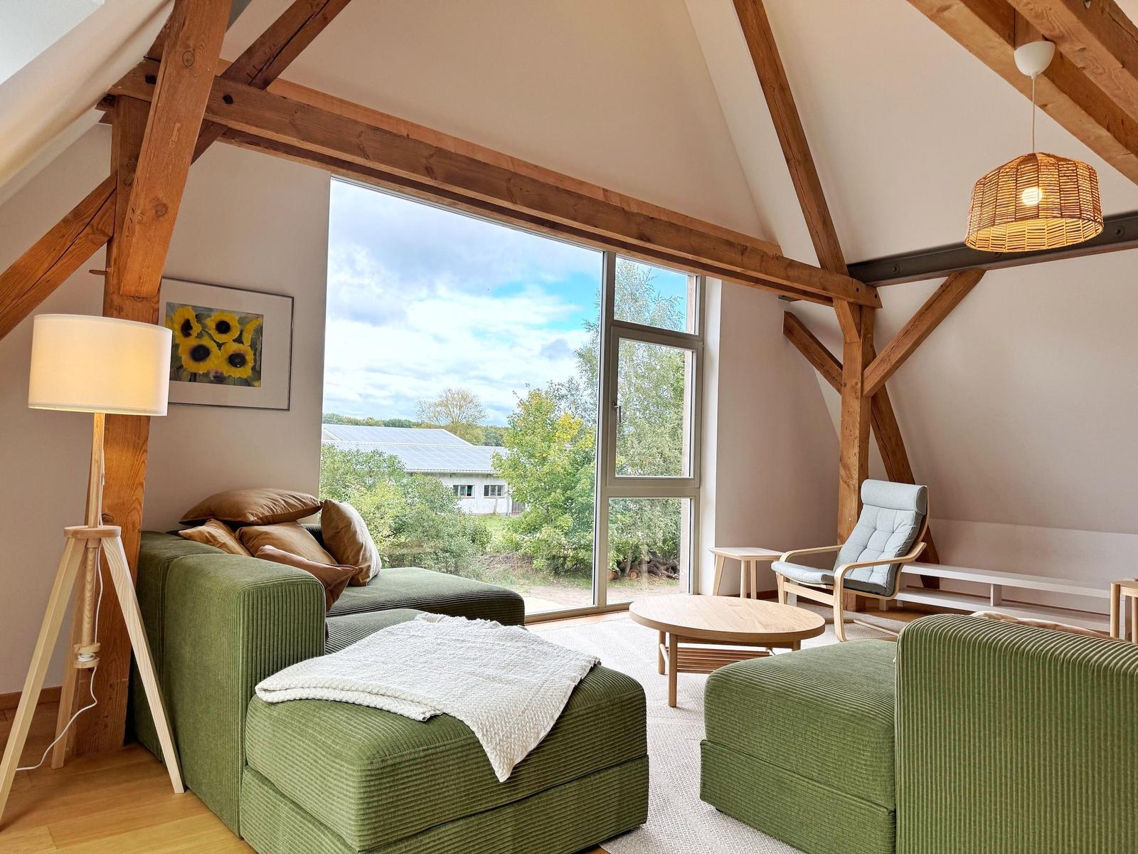 Wohnzimmer mit grünem Sofa, Holzrahmen und großem Fensterblick.