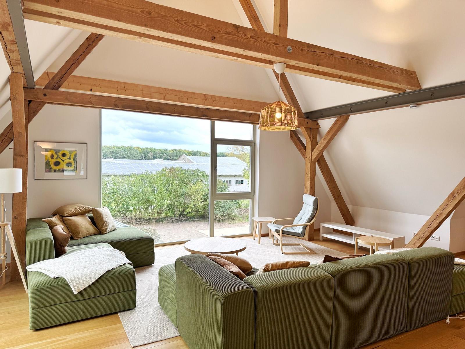 Wohnzimmer mit grünem Sofa, Holzbalken und großem Fensterblick.