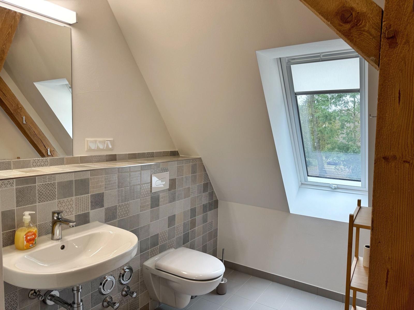 Badezimmer mit Dachfenster, Waschbecken und Toilette unter Holzbalken.