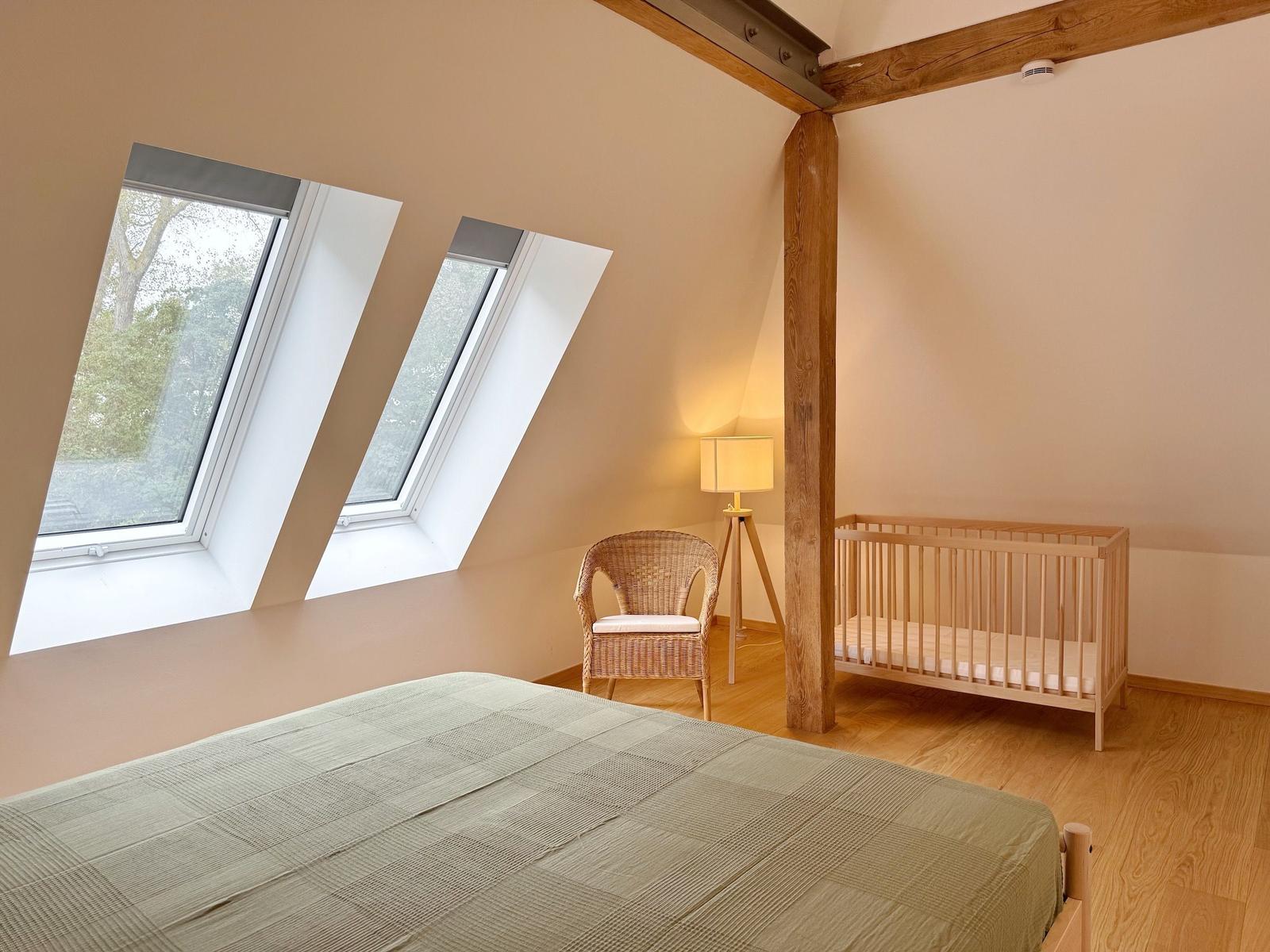 Schlafzimmer mit Babybett, Stuhl und zwei Dachfenstern.