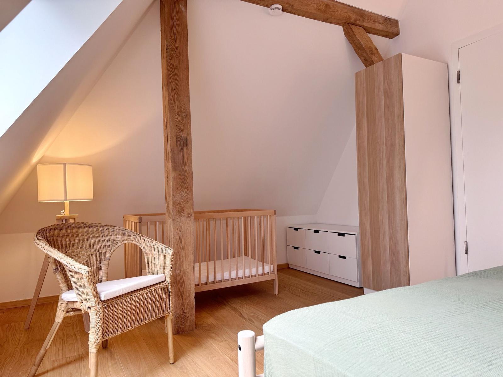 Kinderzimmer mit Babybett, Wickelstuhl und Kleiderschrank unter Dachschrägen.