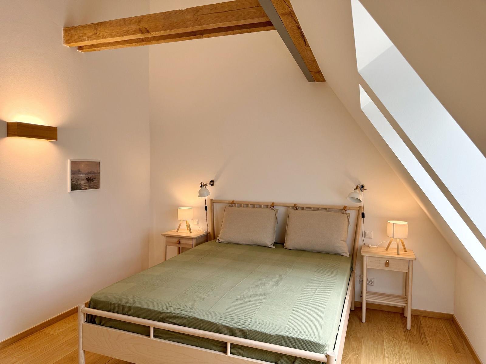 Schlafzimmer mit Dachschräge, Holzbalken und zwei Nachttischen mit Lampen.