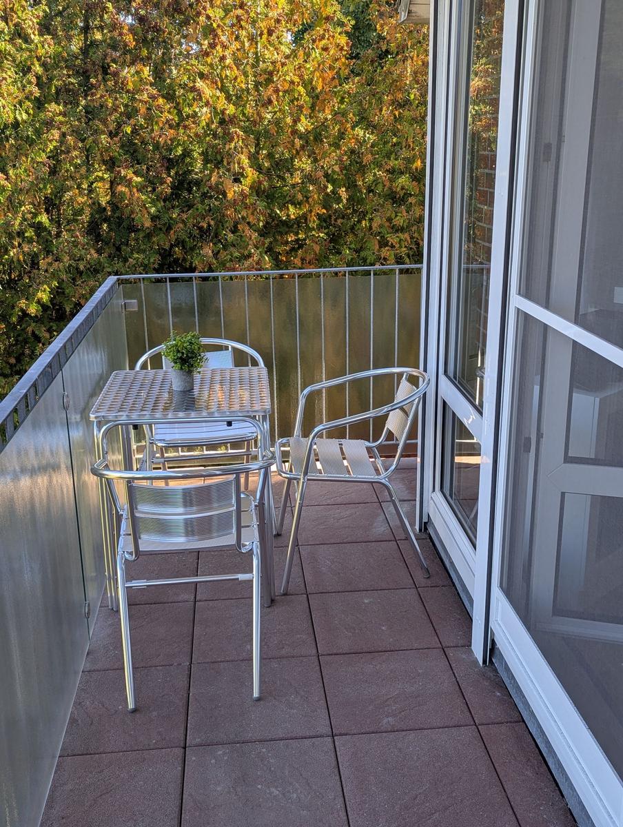 Terrasse mit Metalltisch und Stühlen, umgeben von Bäumen.