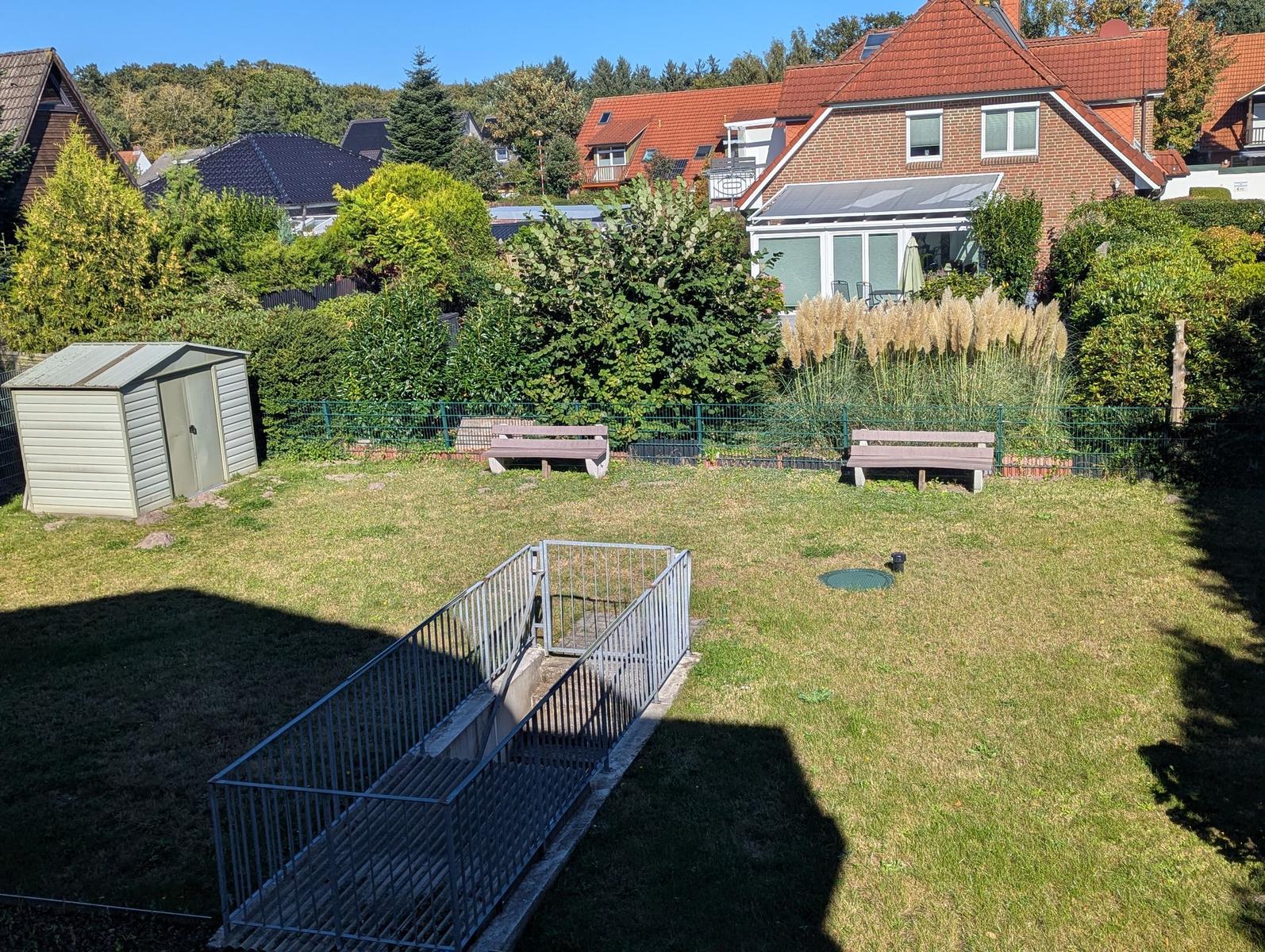 Grüner Garten mit Banken, Schuppen und Rollstuhlgang.