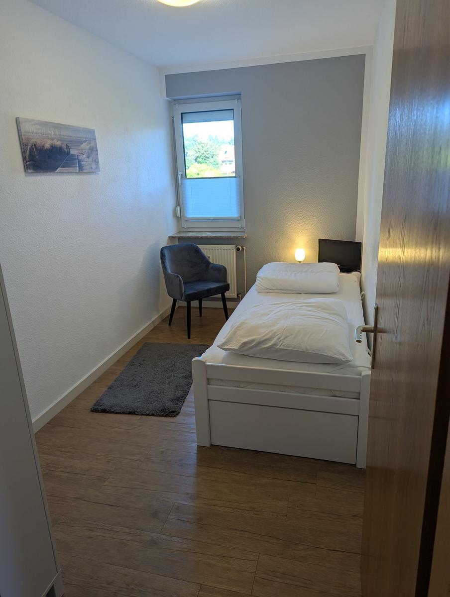 Ein Schlafzimmer mit weißem Bett, Stuhl und Fenster.