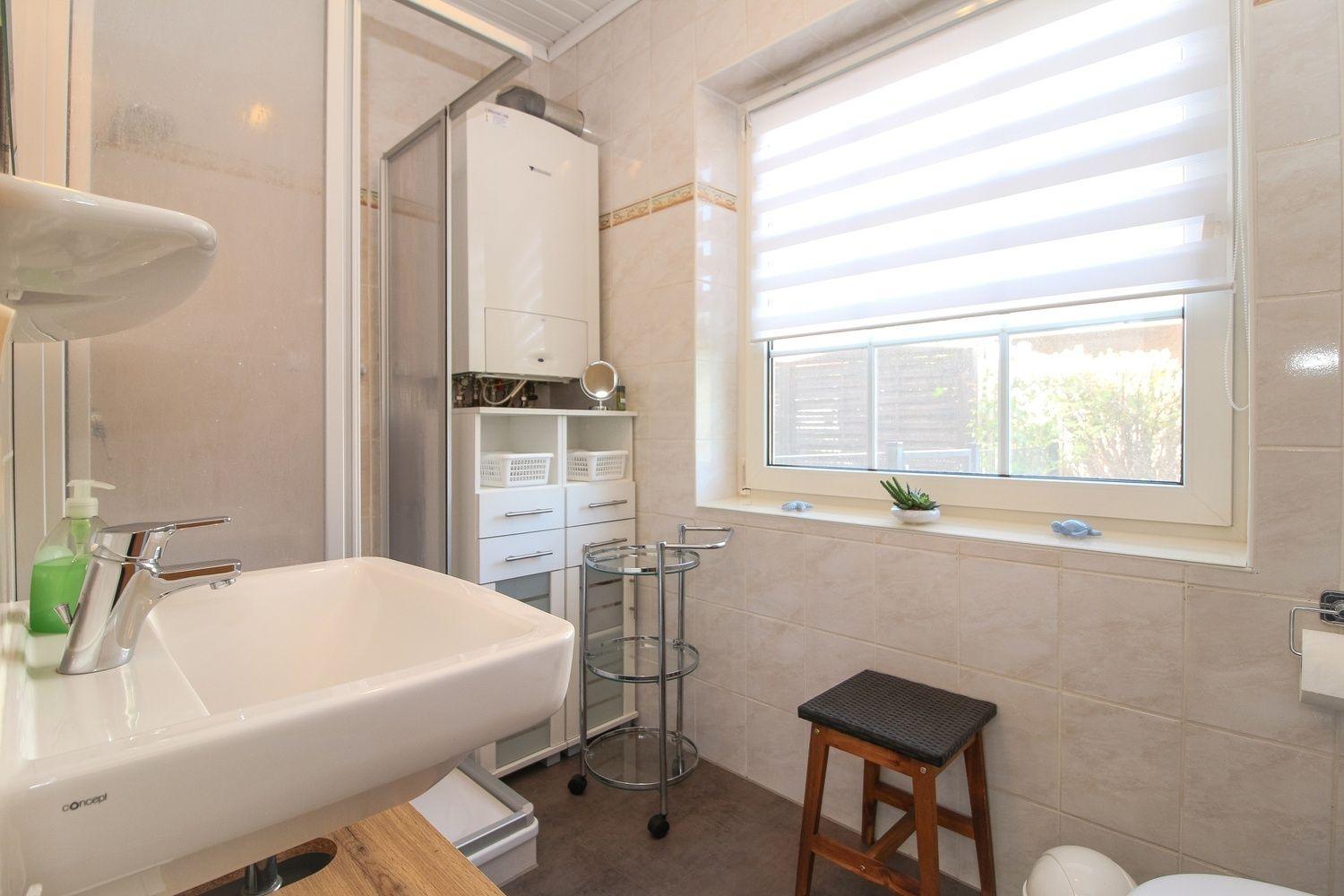 Badezimmer mit Waschbecken, Dusche, Fenster und Stuhl.
